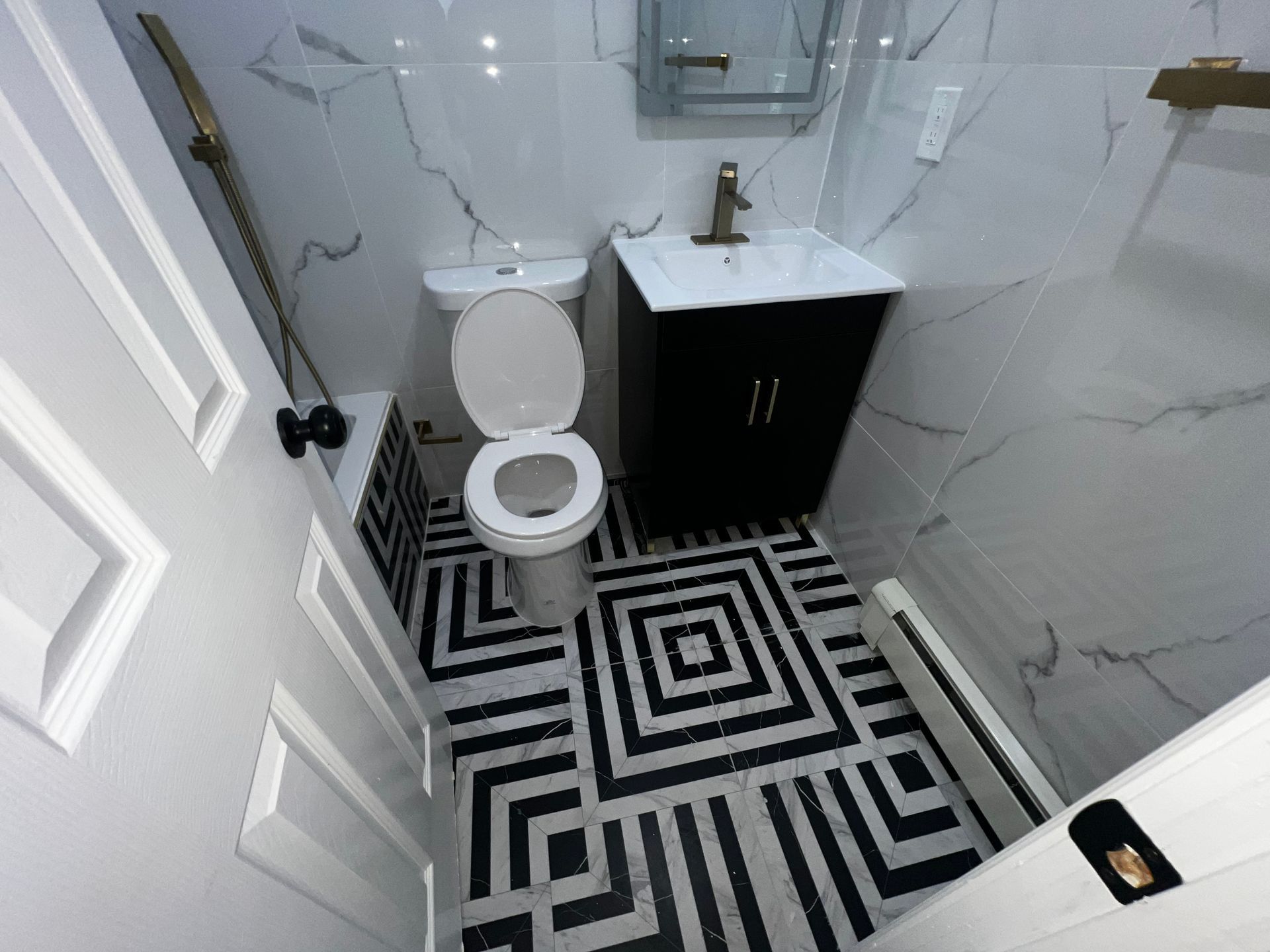 Small modern bathroom with black-and-white geometric floor, toilet, sink vanity, and white tiled walls