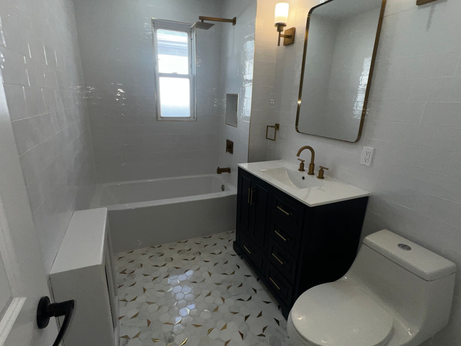 Bright white bathroom with tub-shower, vanity, mirror, toilet, and patterned floor tiles