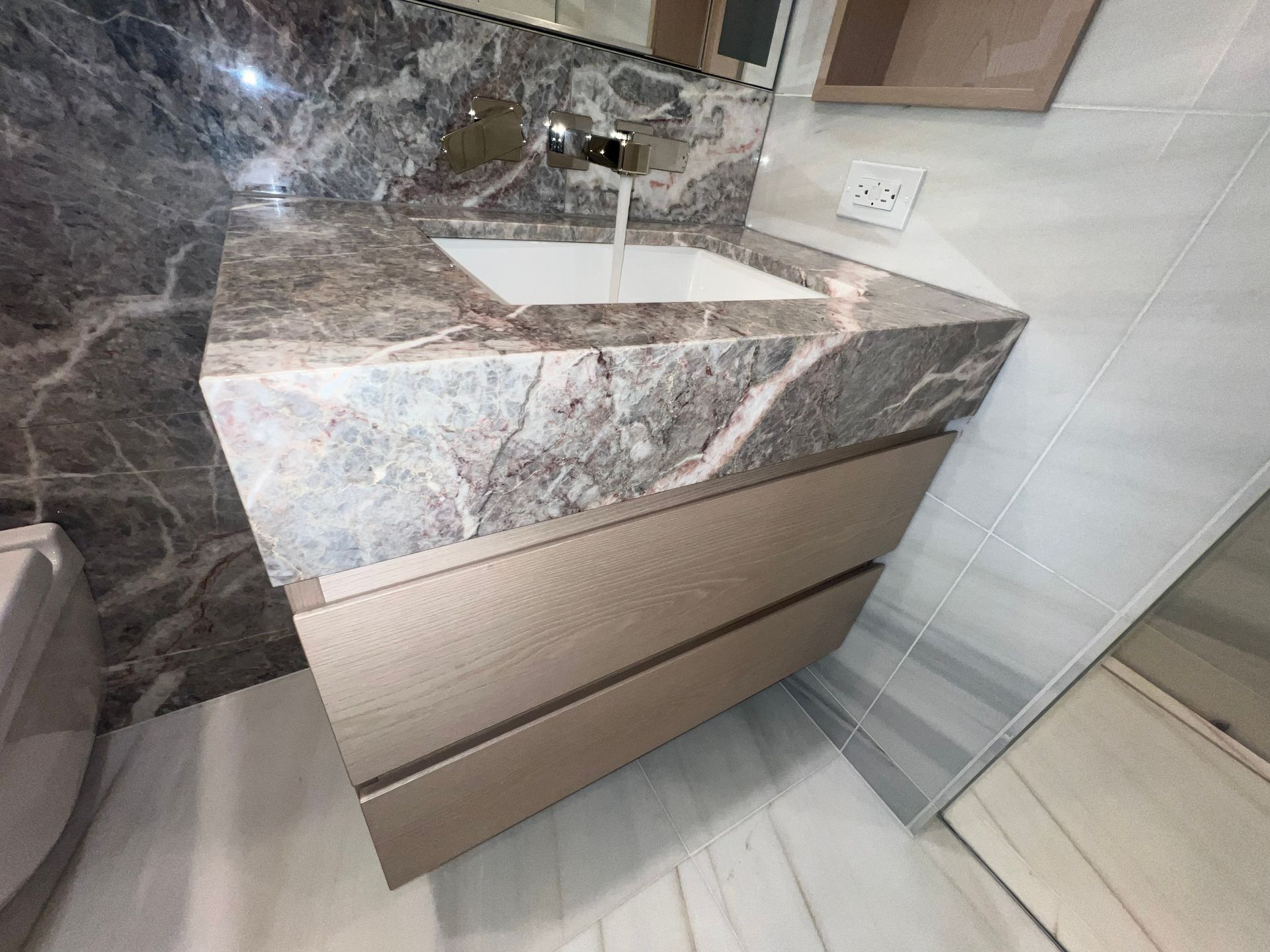 Marble bathroom vanity with sink, brown drawers, and white tile wall