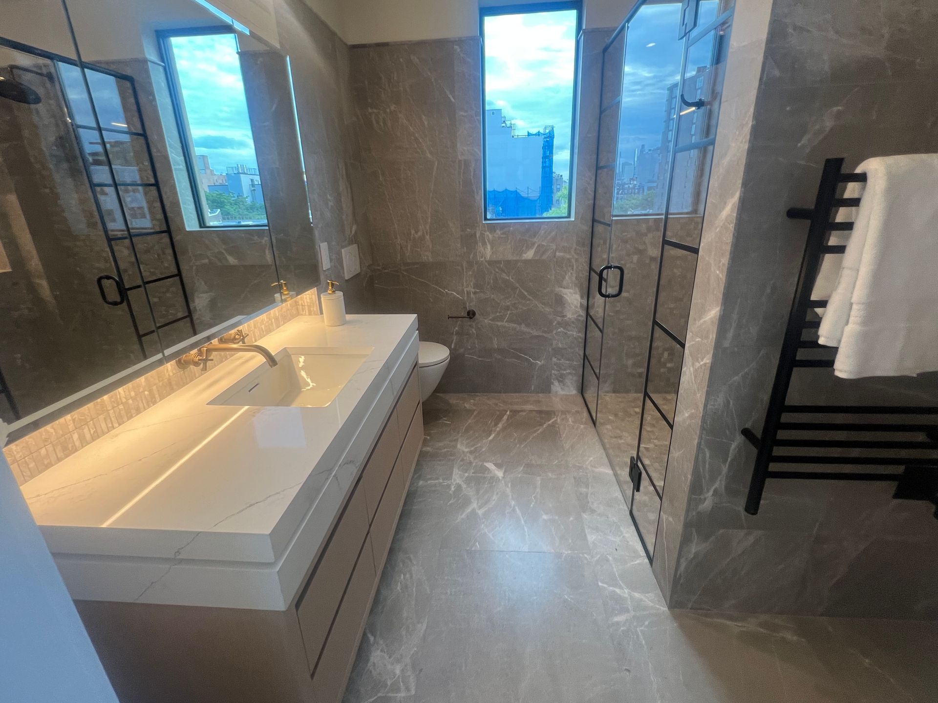 Modern bathroom with double vanity, large mirrors, glass shower, and window with city view