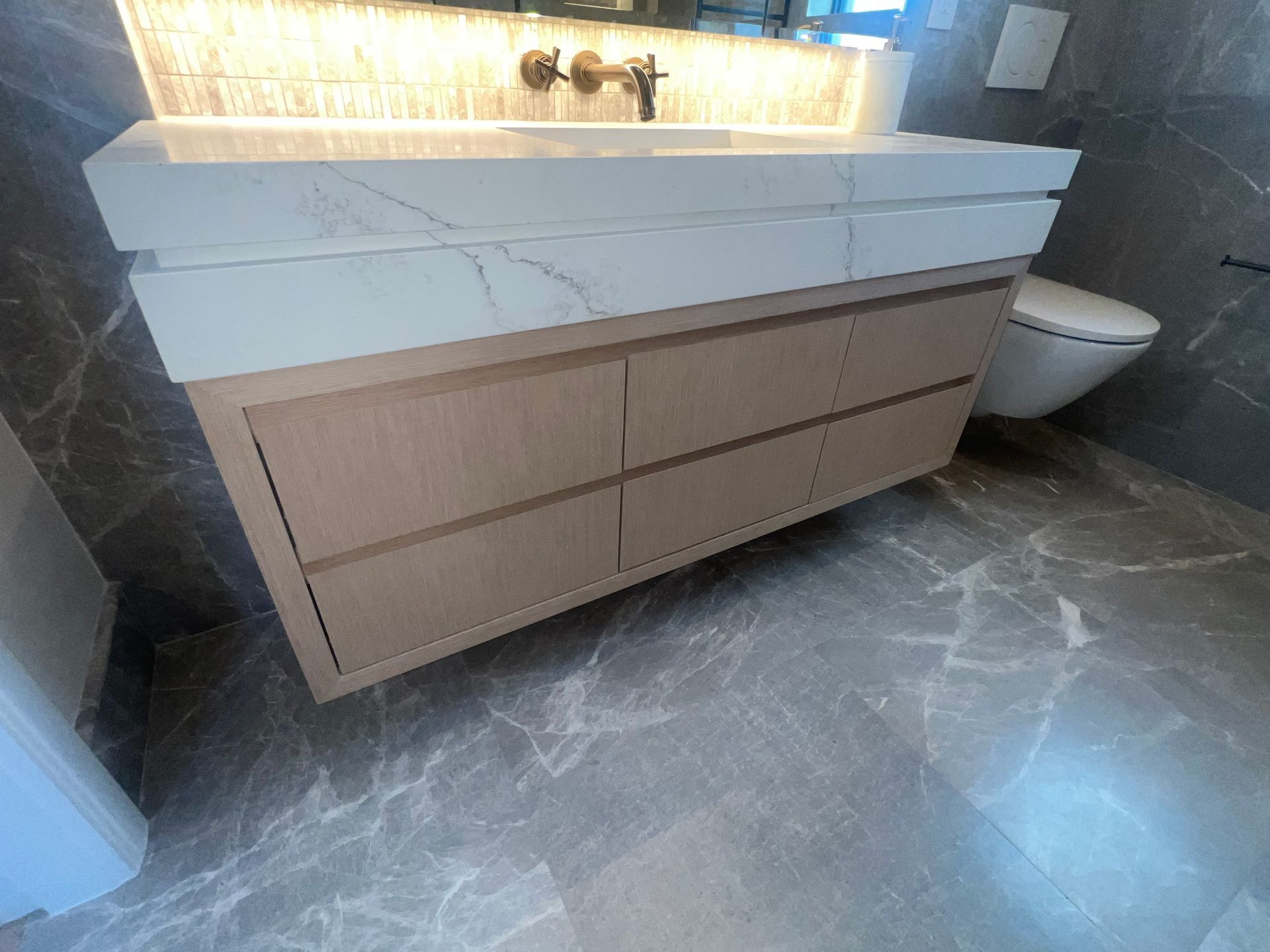Modern bathroom vanity with white stone sink, wood drawers, and illuminated mirror backsplash