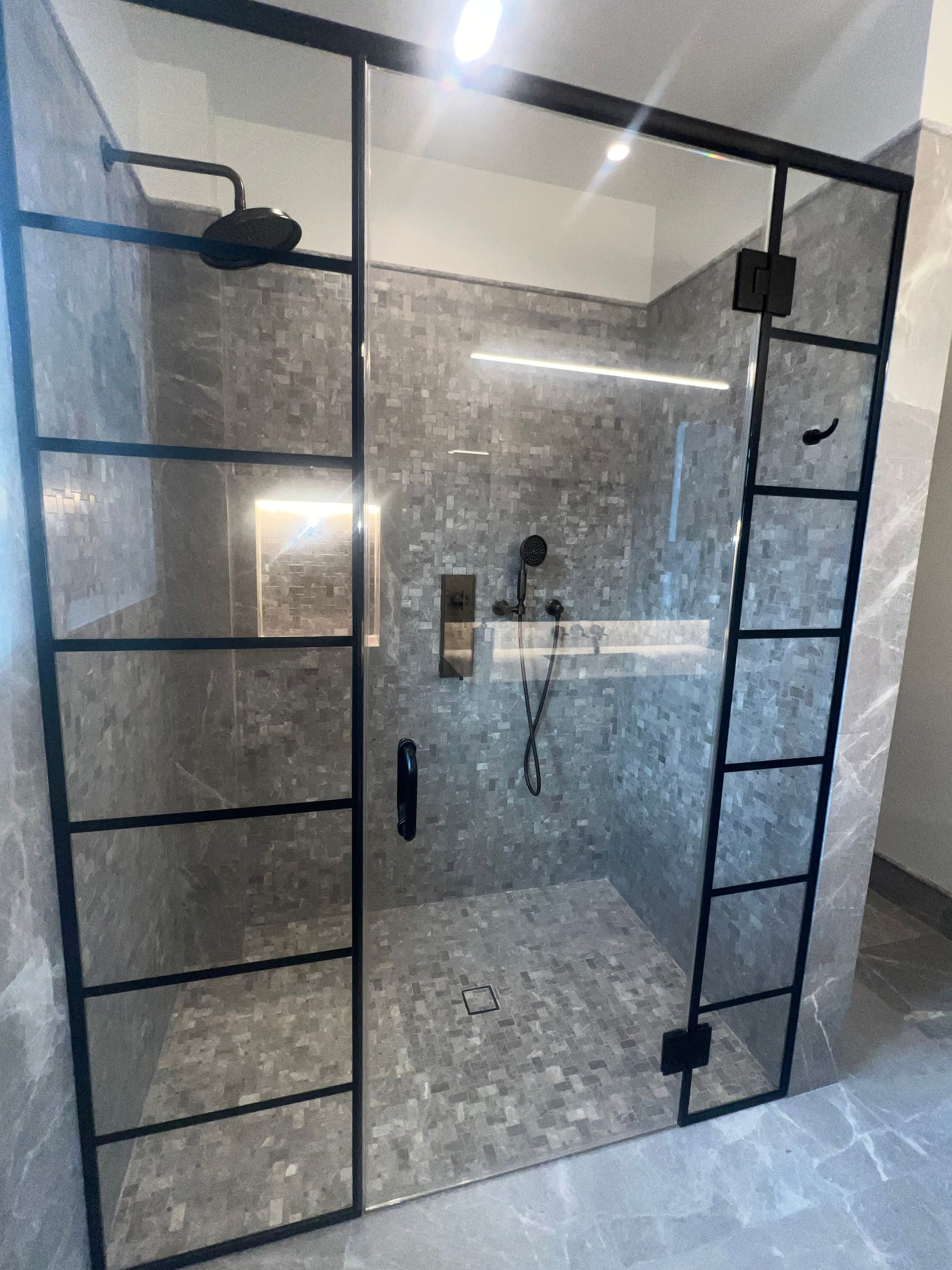 Modern glass shower with black grid framing and a marble-look tiled interior.
