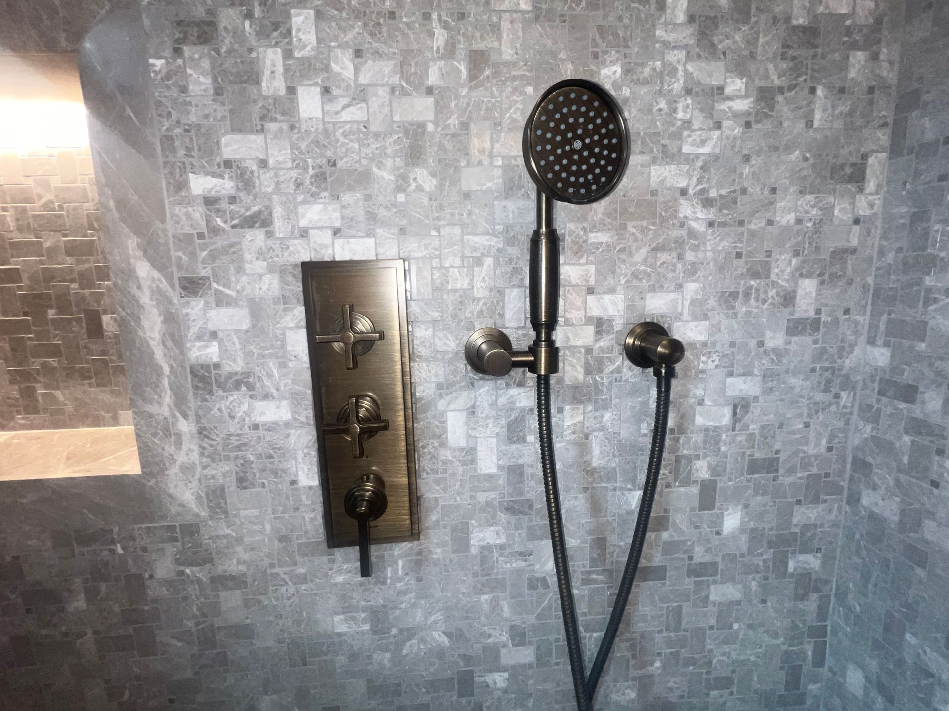 Shower wall with chrome controls, handheld showerhead, and gray tile background