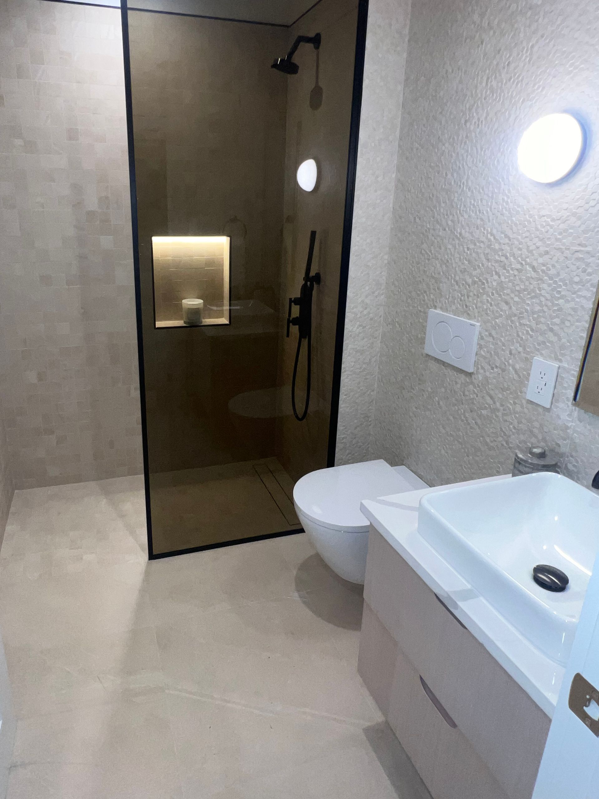 Modern beige bathroom with glass shower, toilet, and white sink vanity