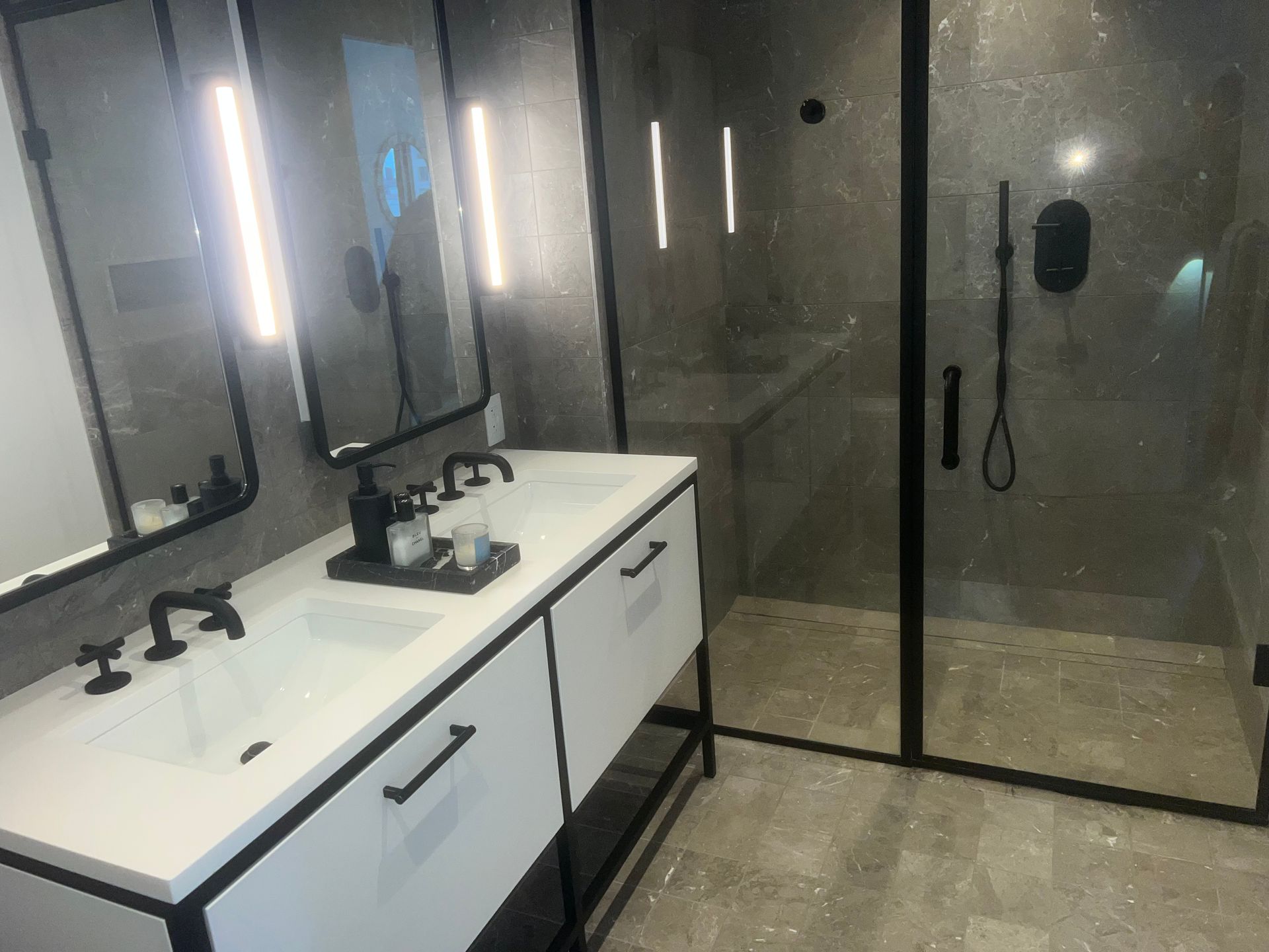 Modern bathroom with double vanity, large mirrors, and glass-enclosed shower in gray and white tones