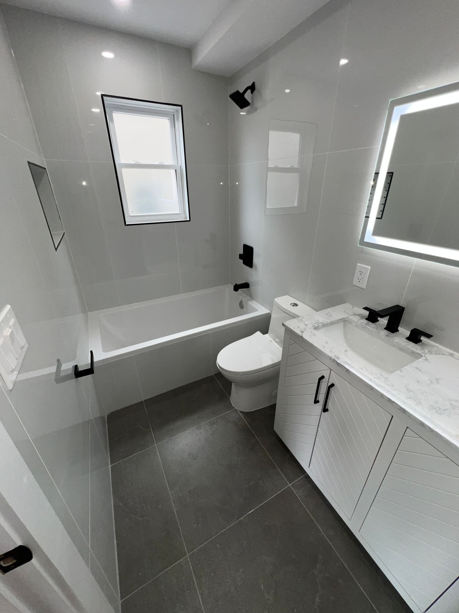 Modern bathroom with white vanity, mirror, toilet, bathtub, and gray tile floor