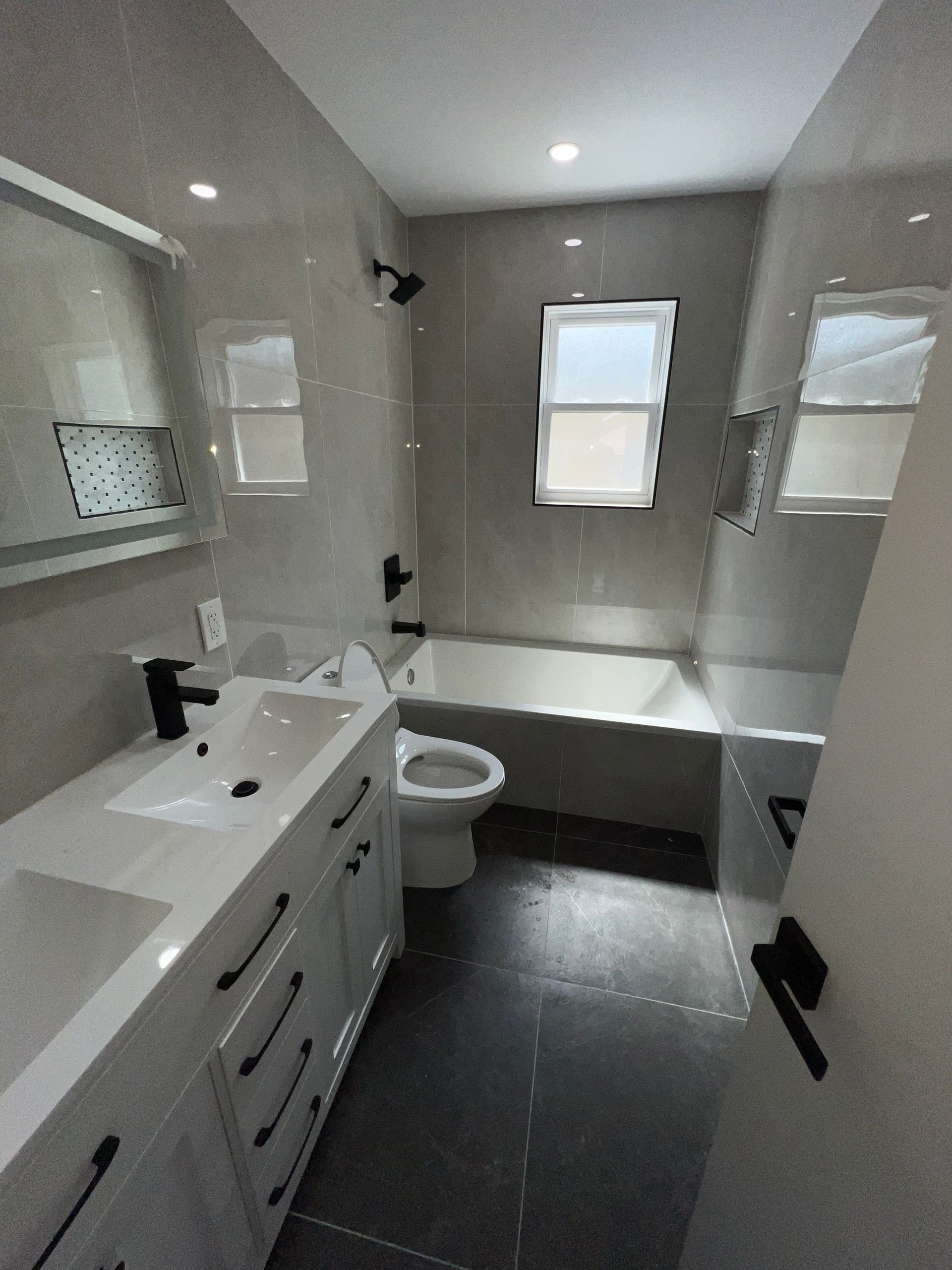 Modern white bathroom with vanity, toilet, bathtub, gray tile floor, and two windows.