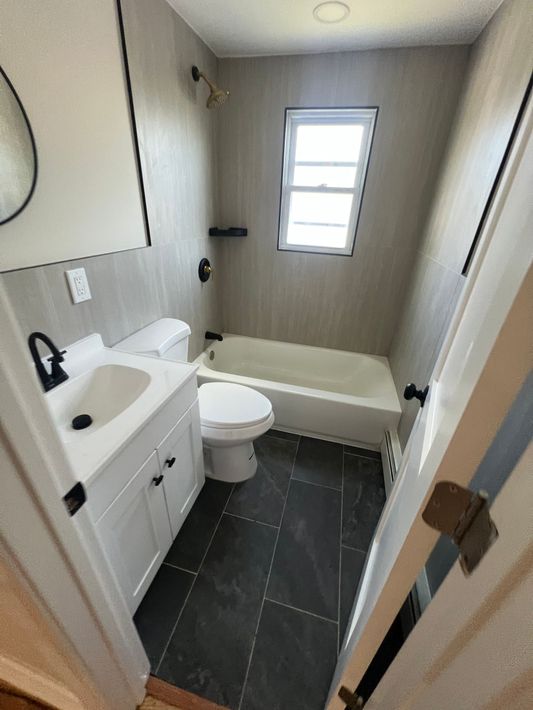 Small bathroom with white vanity, toilet, bathtub, and black tile floor.