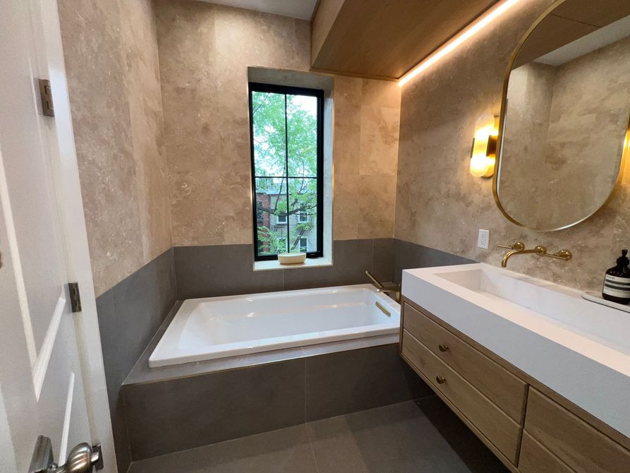 Modern bathroom with a freestanding tub, double vanity, round mirror, and a window with greenery outside