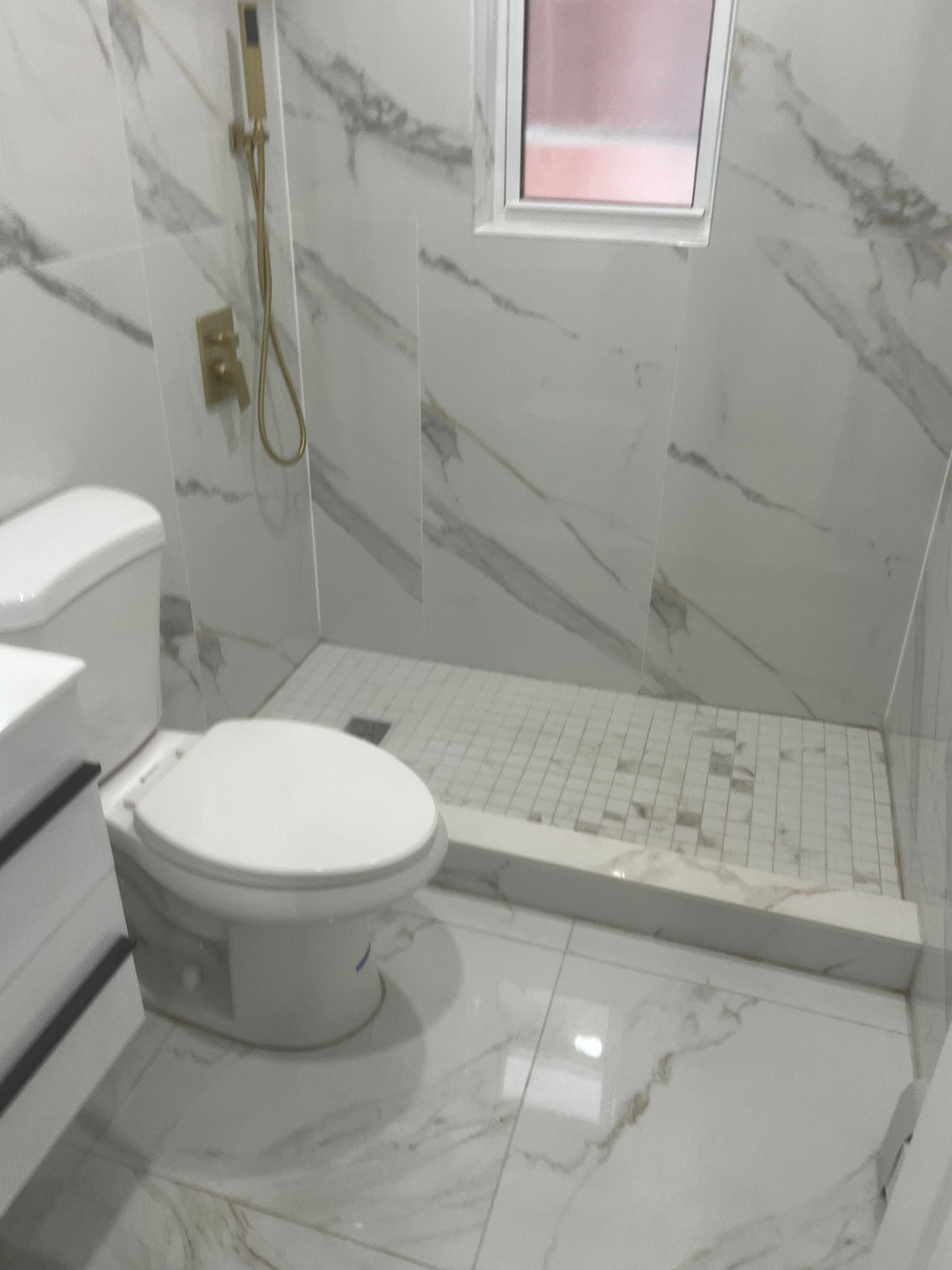Small tiled bathroom with a toilet, walk-in shower, and white-gray marble walls and floor.