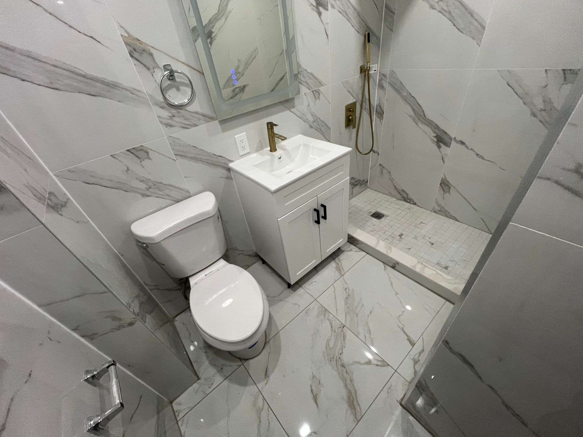 Small white tiled bathroom with toilet, sink vanity, and walk-in shower.