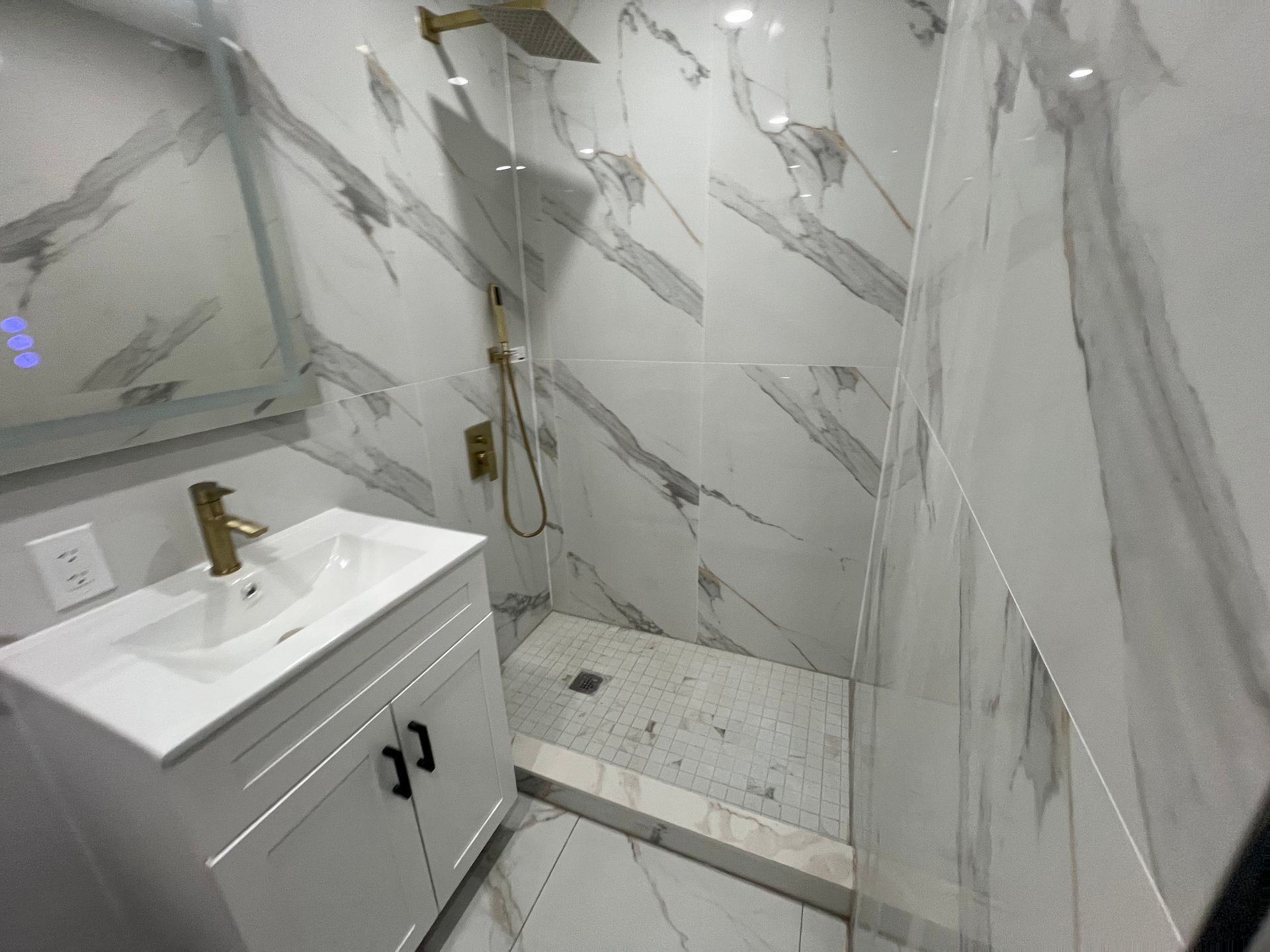 Modern bathroom with marble-look tile, white vanity, brass faucet, and walk-in shower.