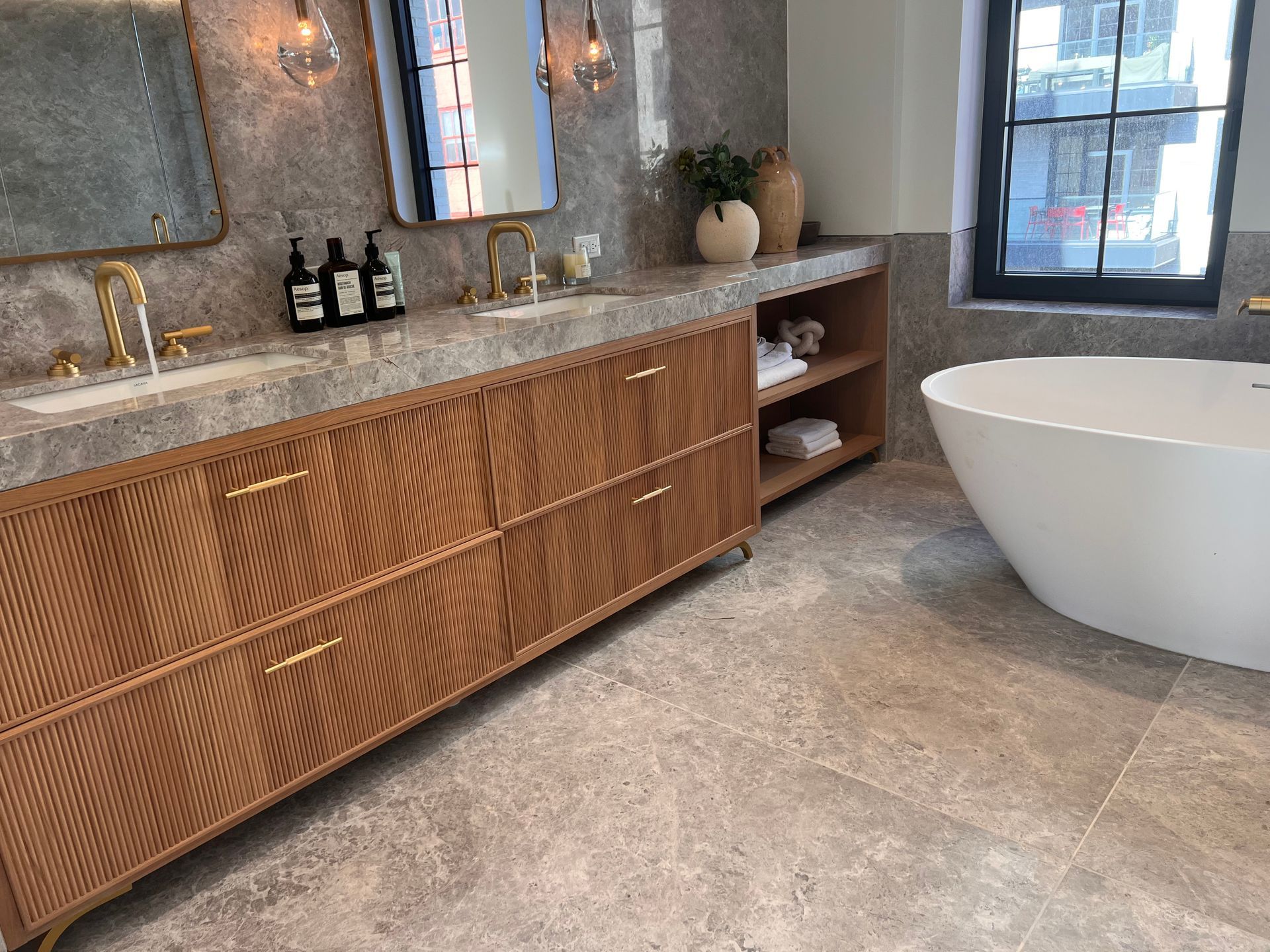 Modern bathroom with wood vanity, stone countertop, and freestanding white tub by a window