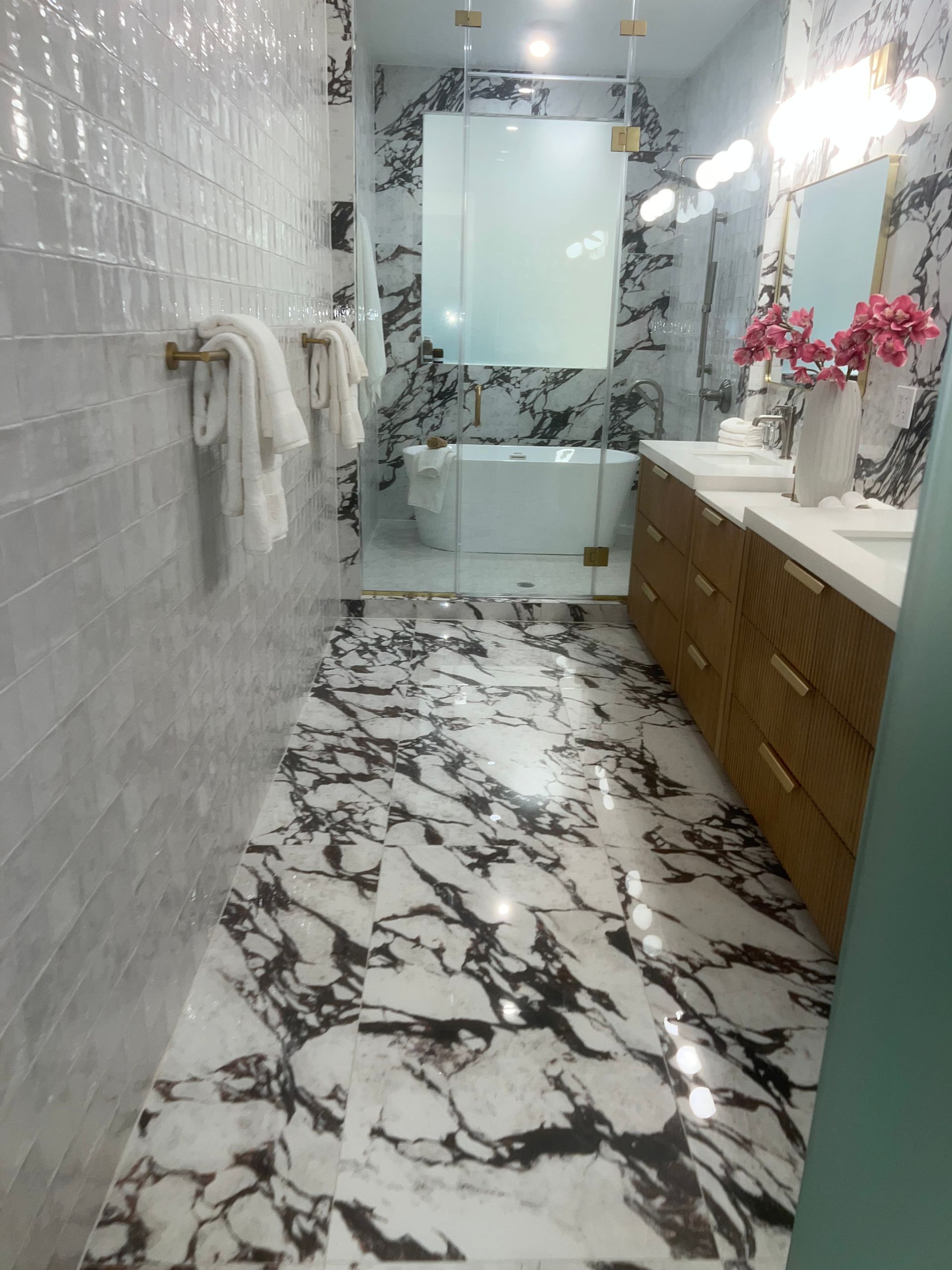 Modern bathroom with marble-pattern floor and walls, glass shower door, wood vanity, and pink flowers