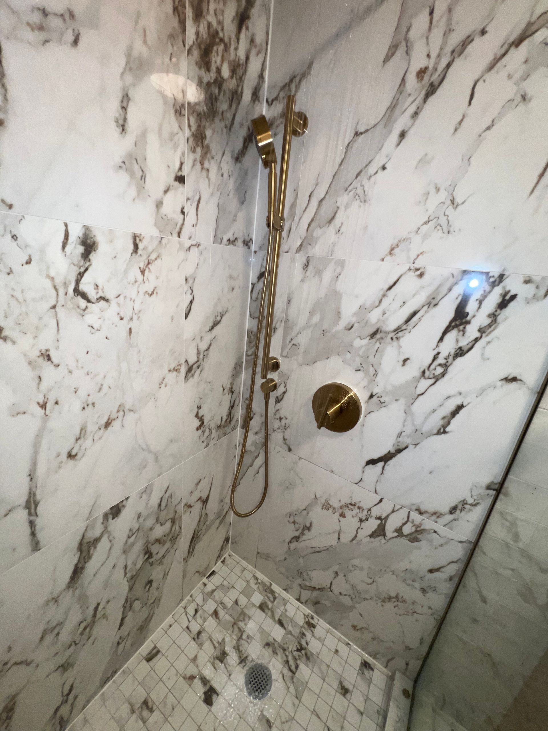 Marble-tiled shower corner with brass fixtures and handheld showerhead