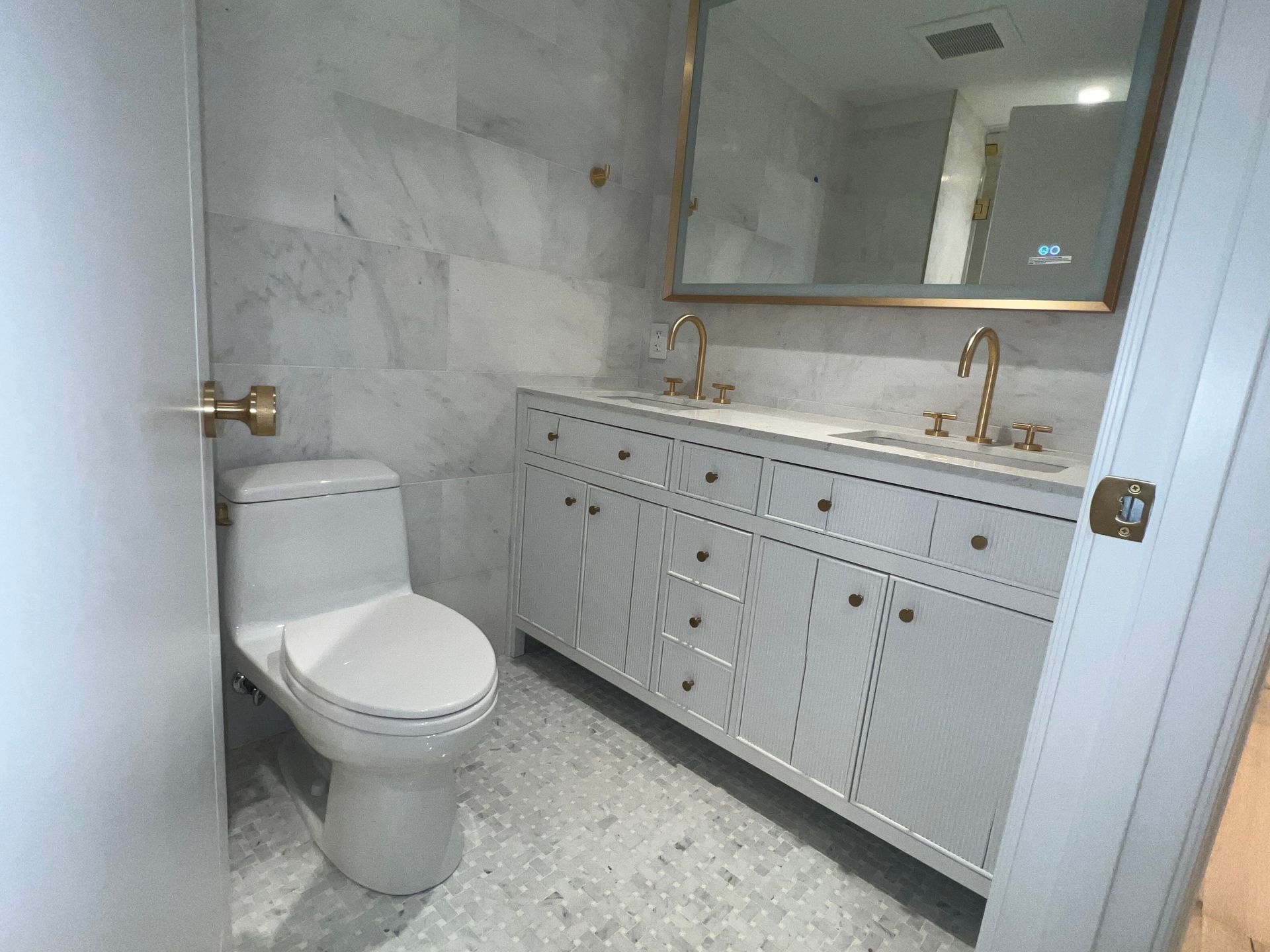 Modern bathroom with white marble walls, toilet, double vanity, and large mirror