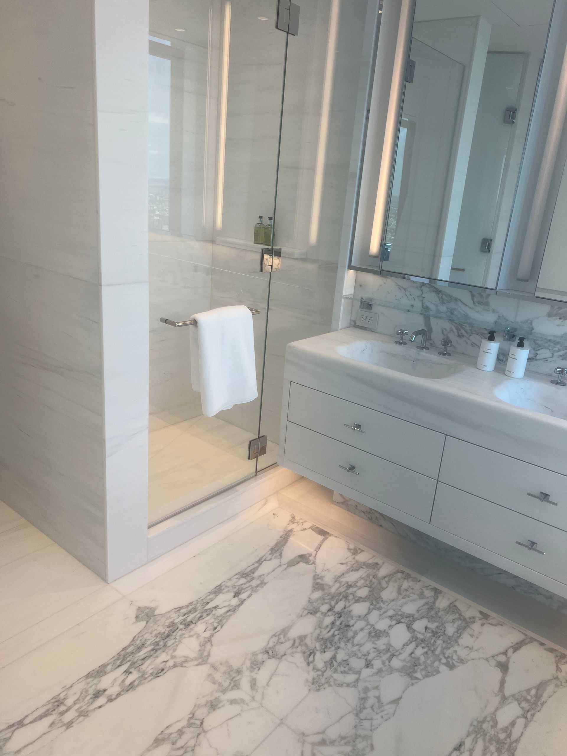 Bright marble bathroom with glass shower, double vanity, and white towel on a chrome bar