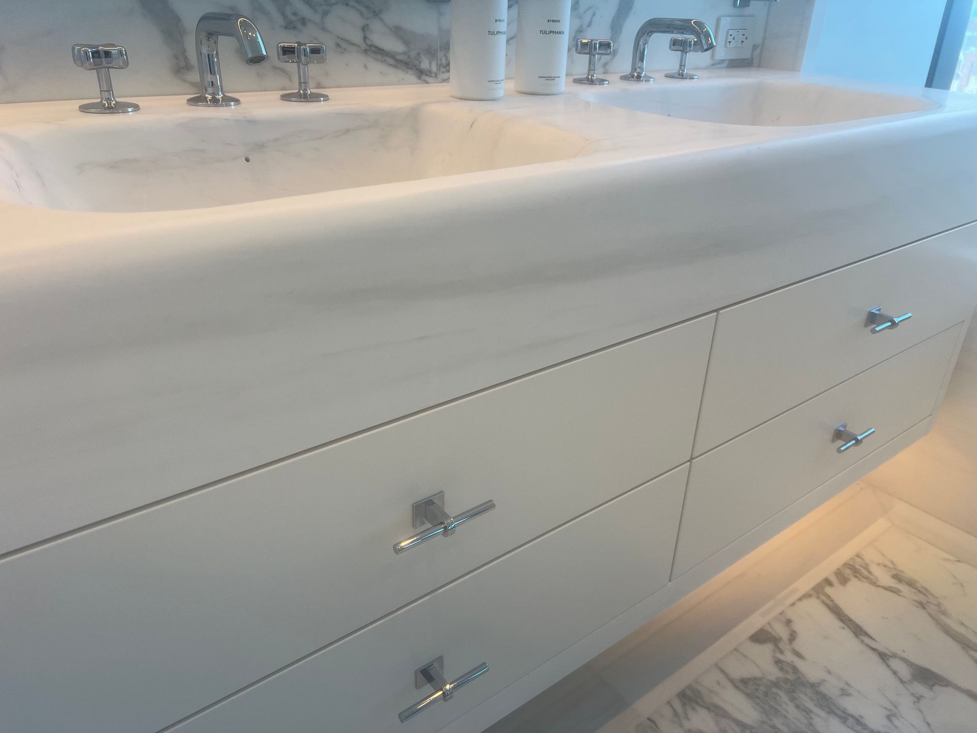 Modern white bathroom vanity with marble countertop, chrome faucets, and built-in drawers