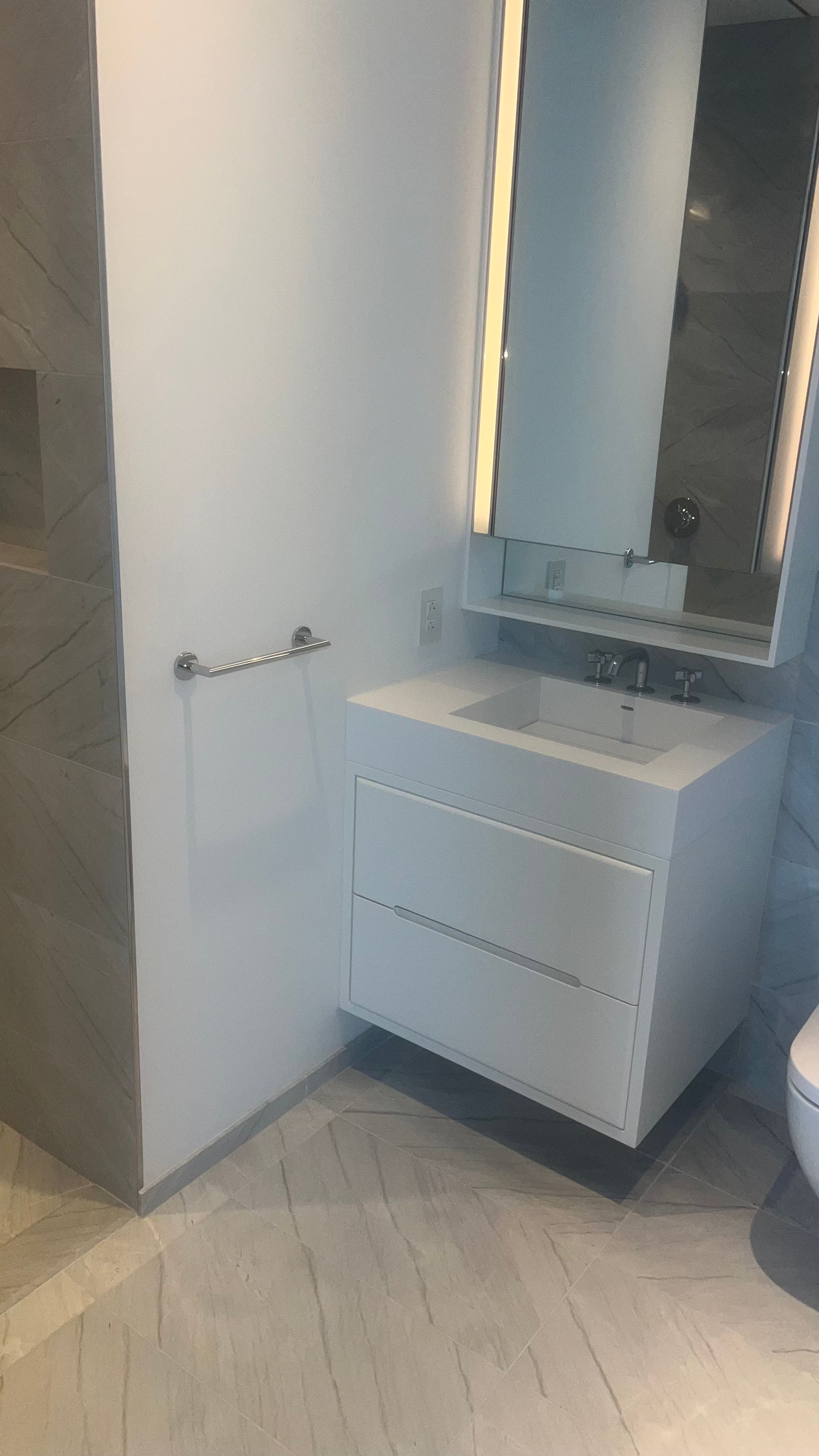 Modern bathroom vanity with white drawers, sink, mirror, and gray tiled floor.