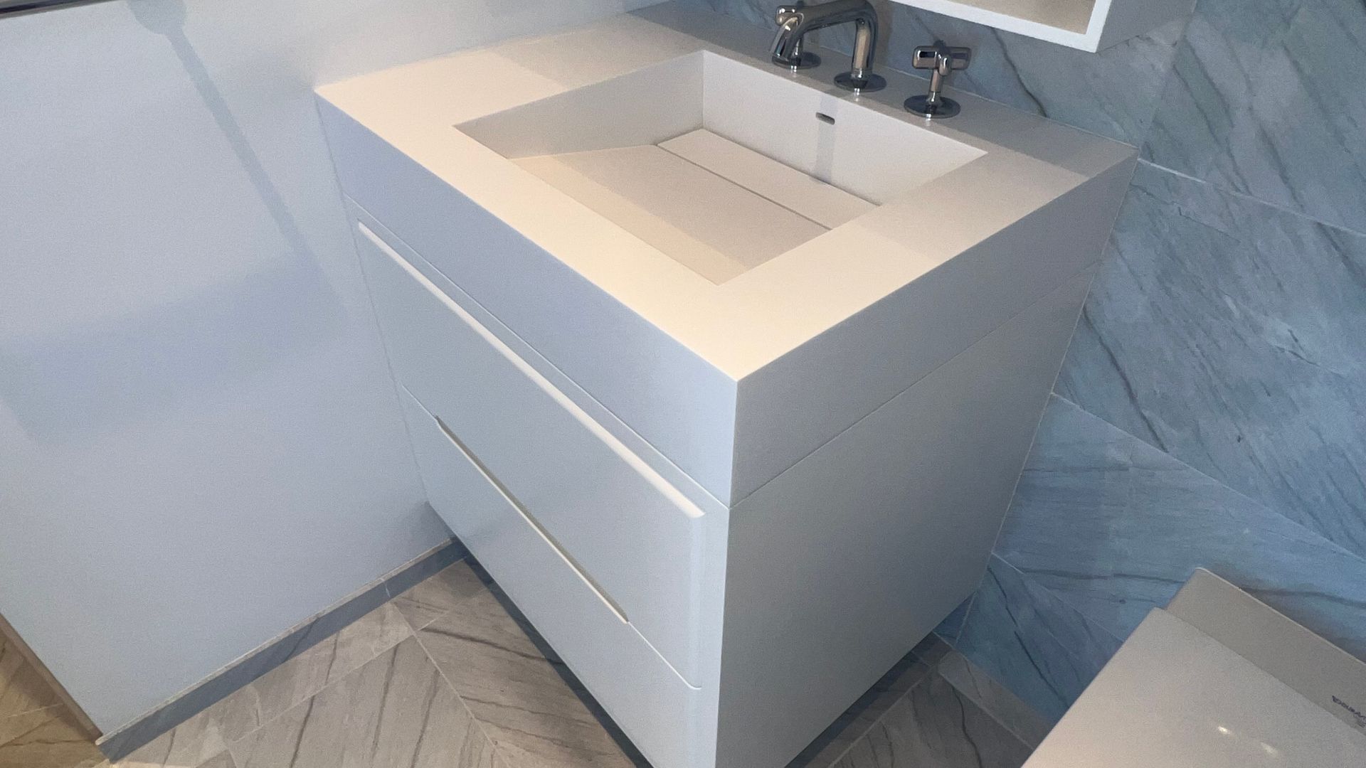White bathroom vanity with sink and chrome faucet in a tiled corner.