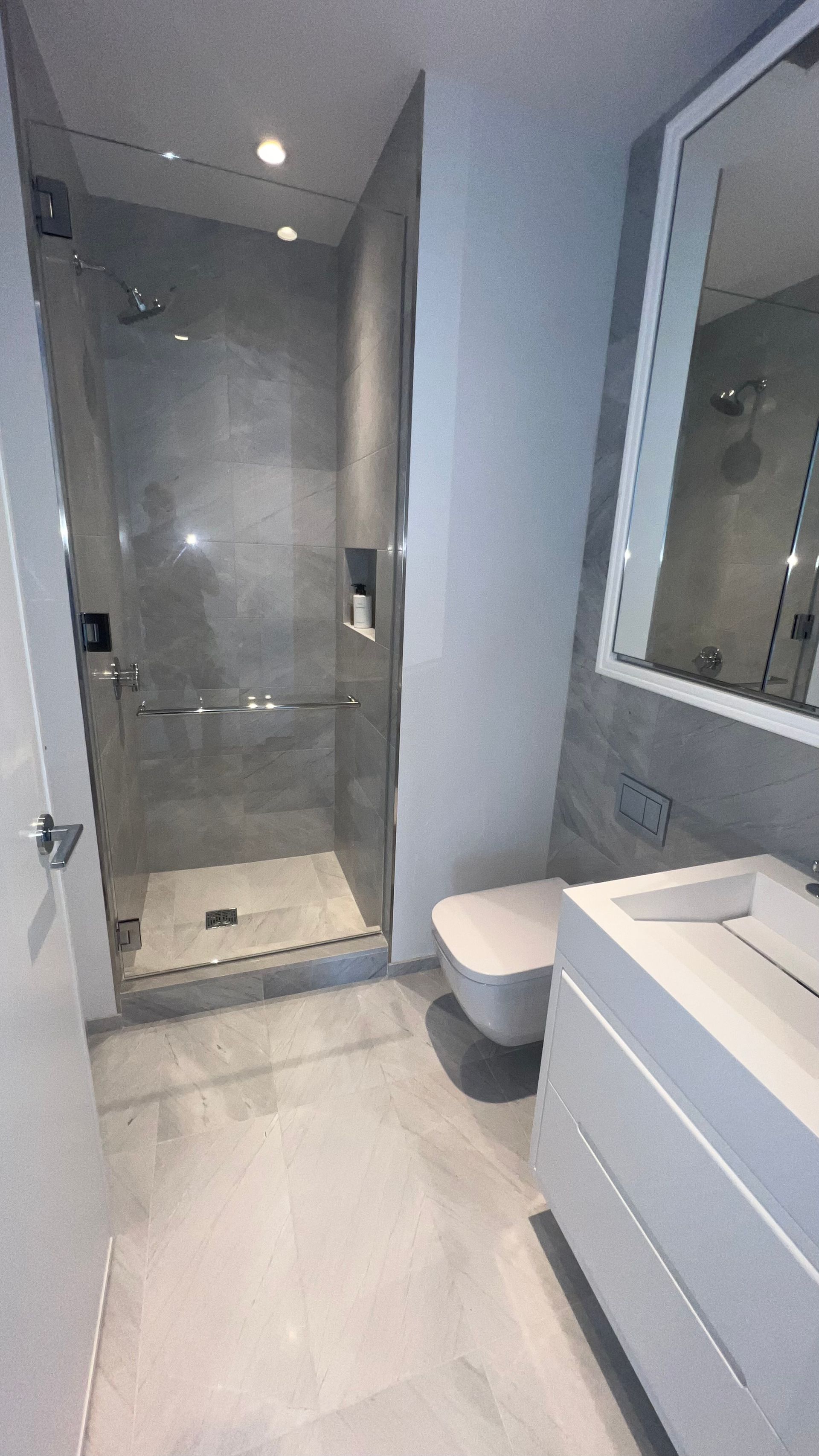 Modern bathroom with glass shower, gray tiles, white vanity, and wall mirror