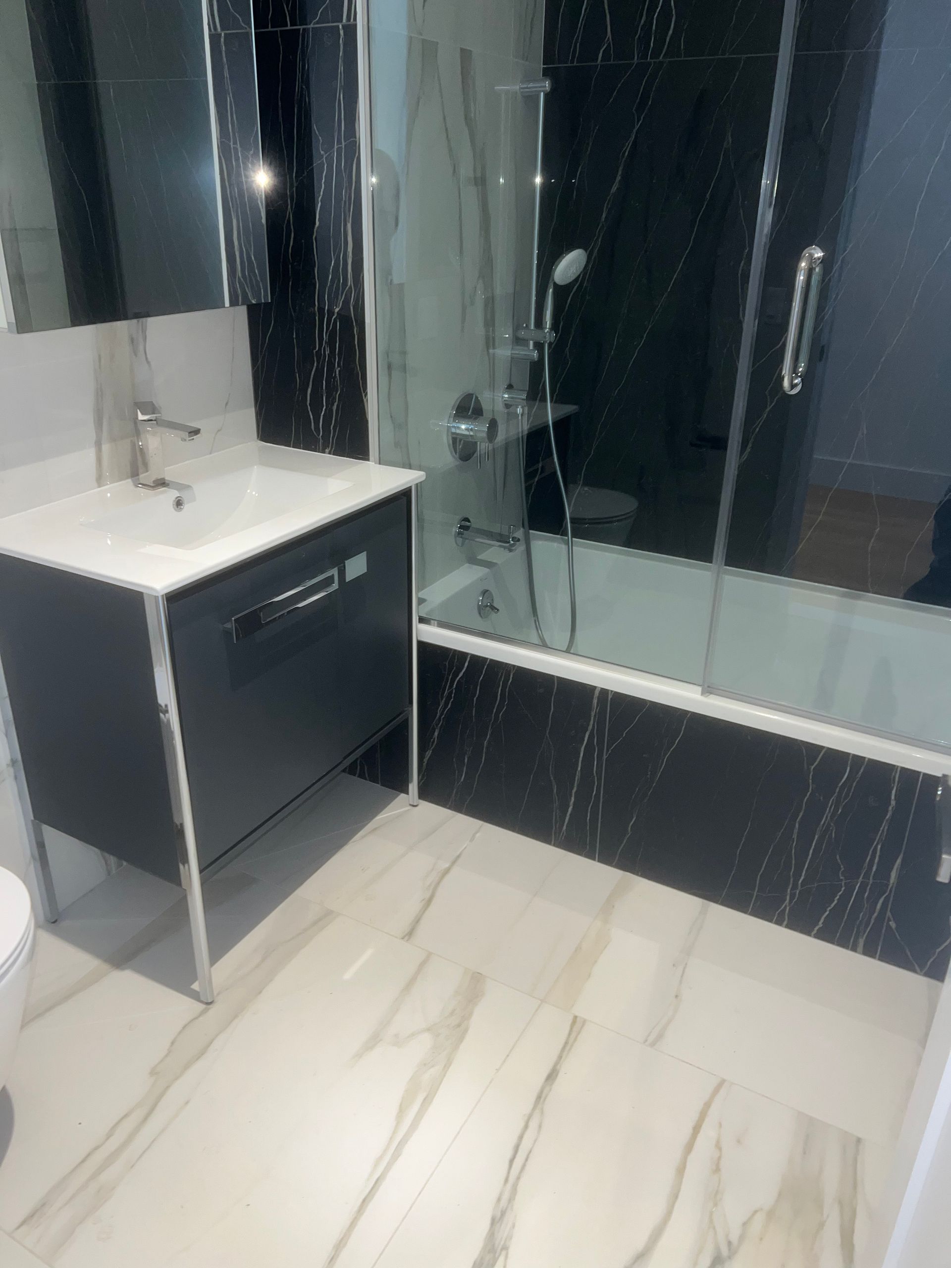 Modern bathroom with black vanity, white sink, glass shower, and marble-pattern tile flooring