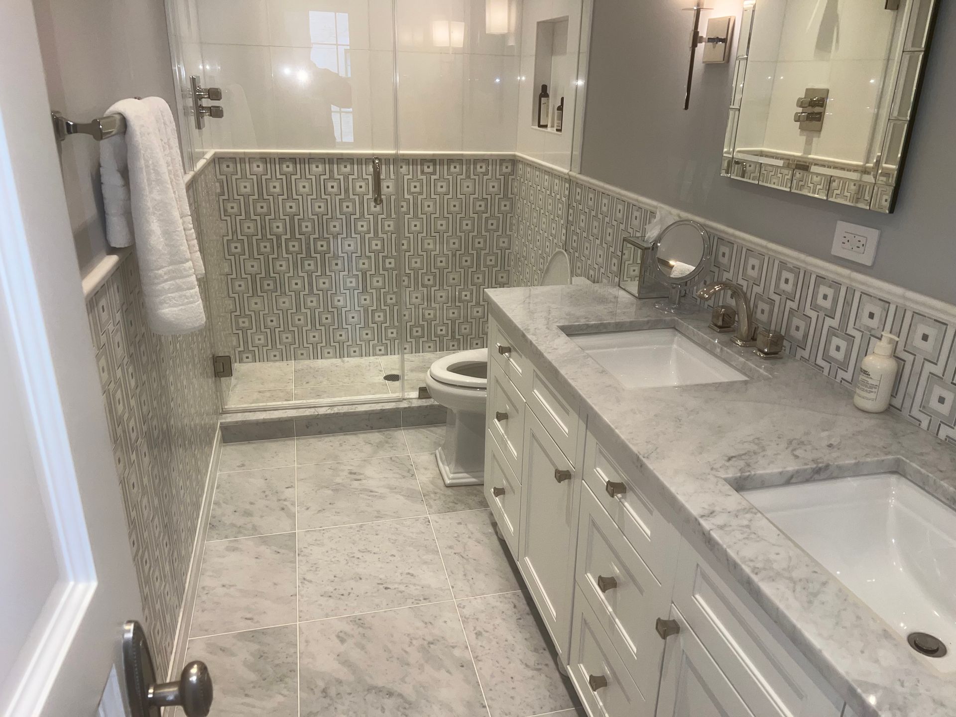 Accessible bathroom with double sinks, large mirror, and walk-in shower with patterned tile walls