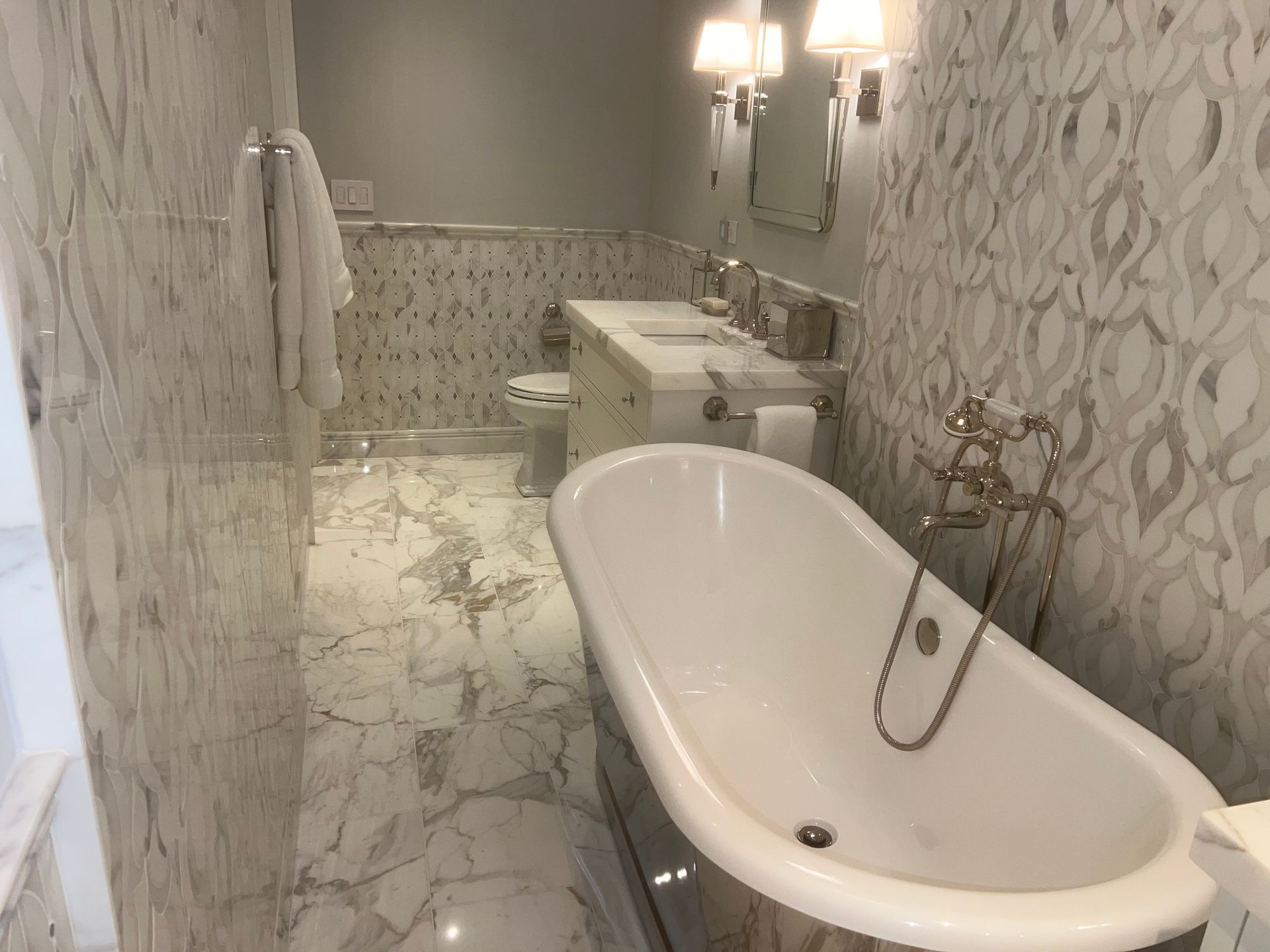 Elegant marble bathroom with a clawfoot tub, vanity, sink, and wall sconces