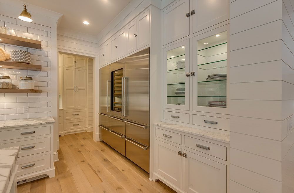 Bright white kitchen with built-in stainless appliances, wood floors, and glass-front cabinets