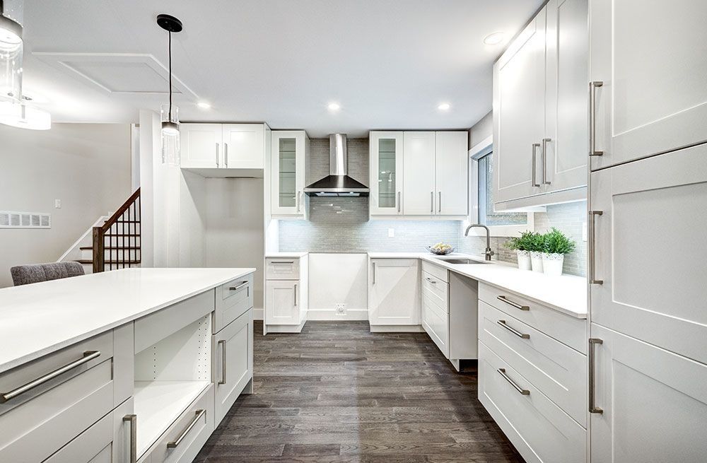Bright white modern kitchen with island, dark wood floors, and stainless steel range hood