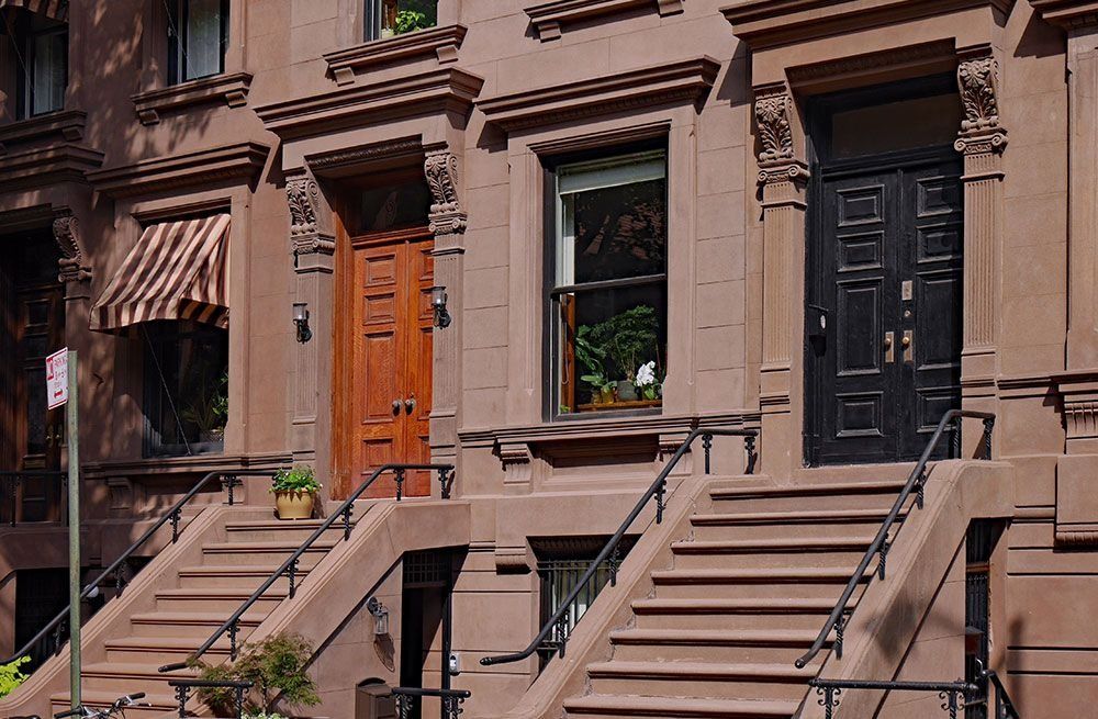Brownstone row houses with brown and black doors, stoops, and potted plants on a city street