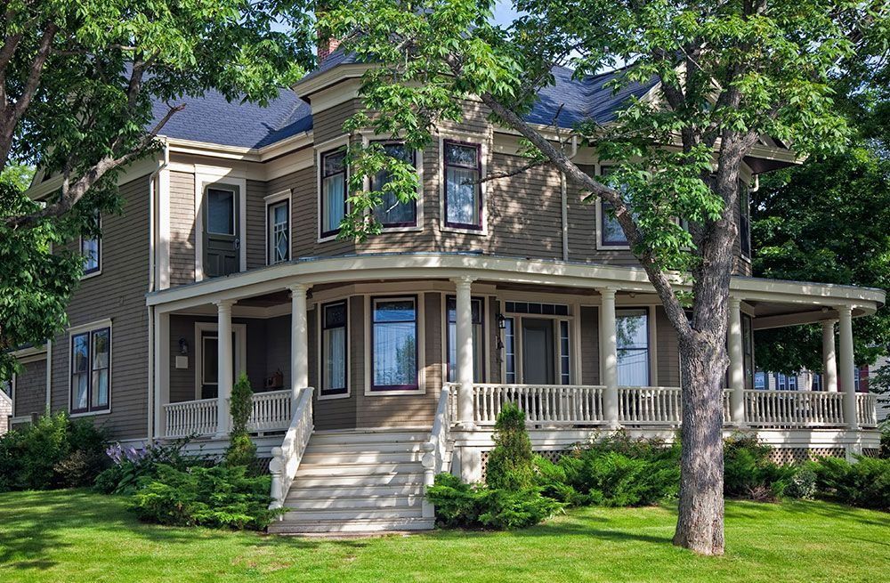 Two-story house with a wraparound porch, white trim, and trees in a green yard
