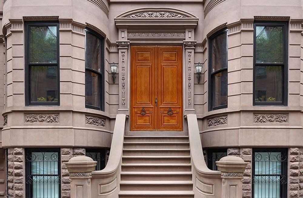 Front entrance of a brownstone with stone steps and a wooden double door, flanked by tall windows