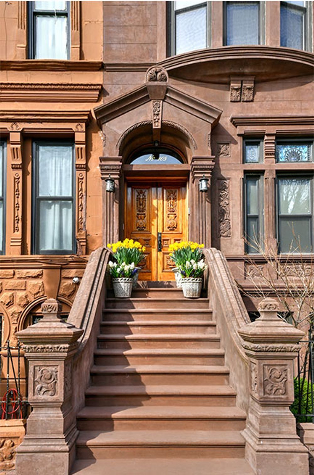 Brown brownstone townhouse entrance with stoop, wooden door, and flower pots