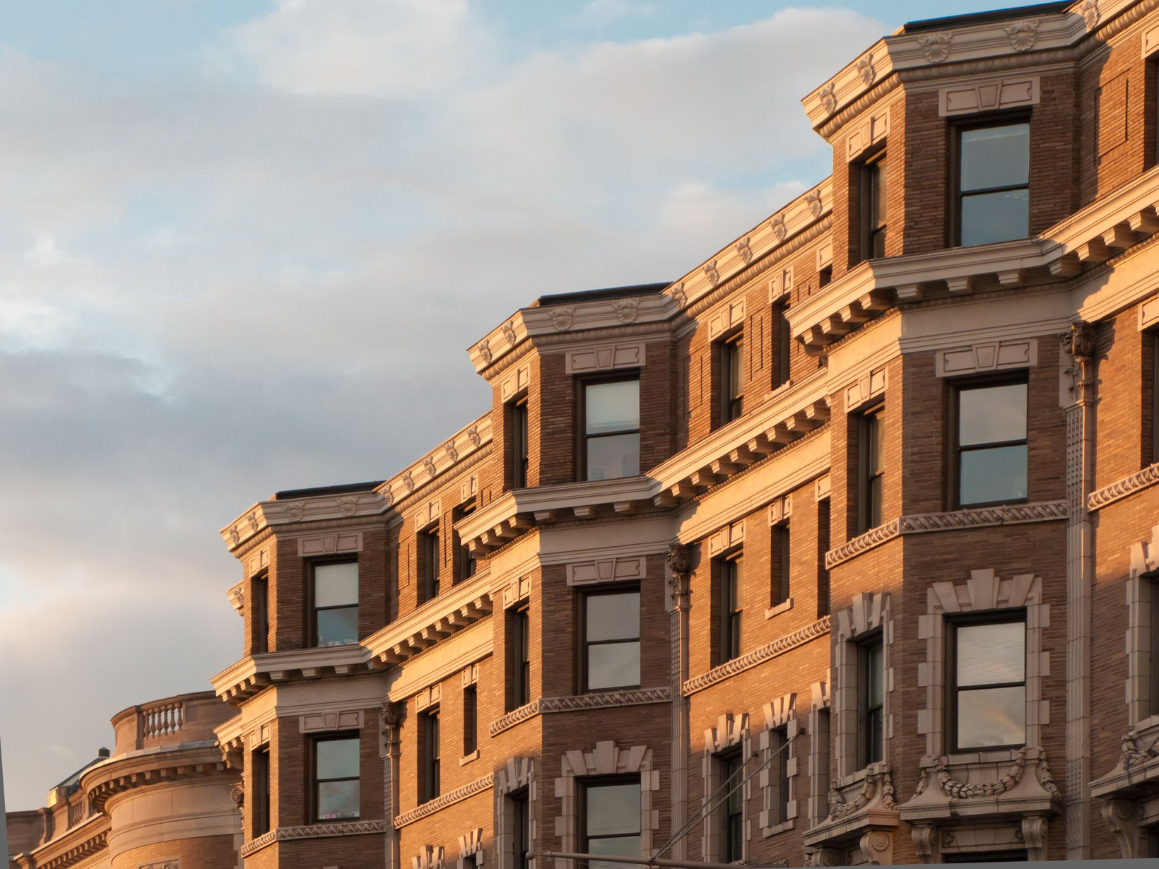 Row of brown brick apartment buildings with ornate facades under a soft evening sky