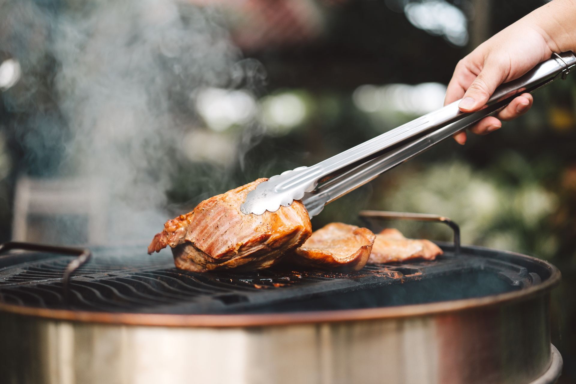 Hand placing grilled steak on a barbecue grill with smoke rising
