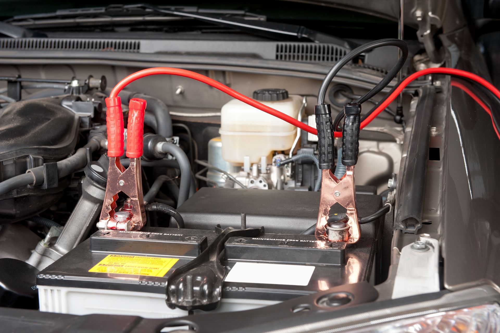 Car engine bay with jumper cables connected to the battery for a jump start