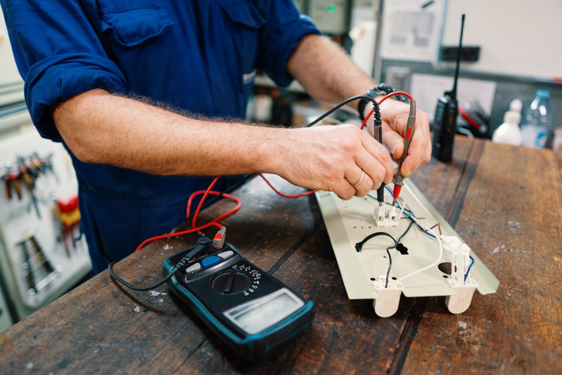 Person testing an electrical circuit on a workbench with a multimeter and wires