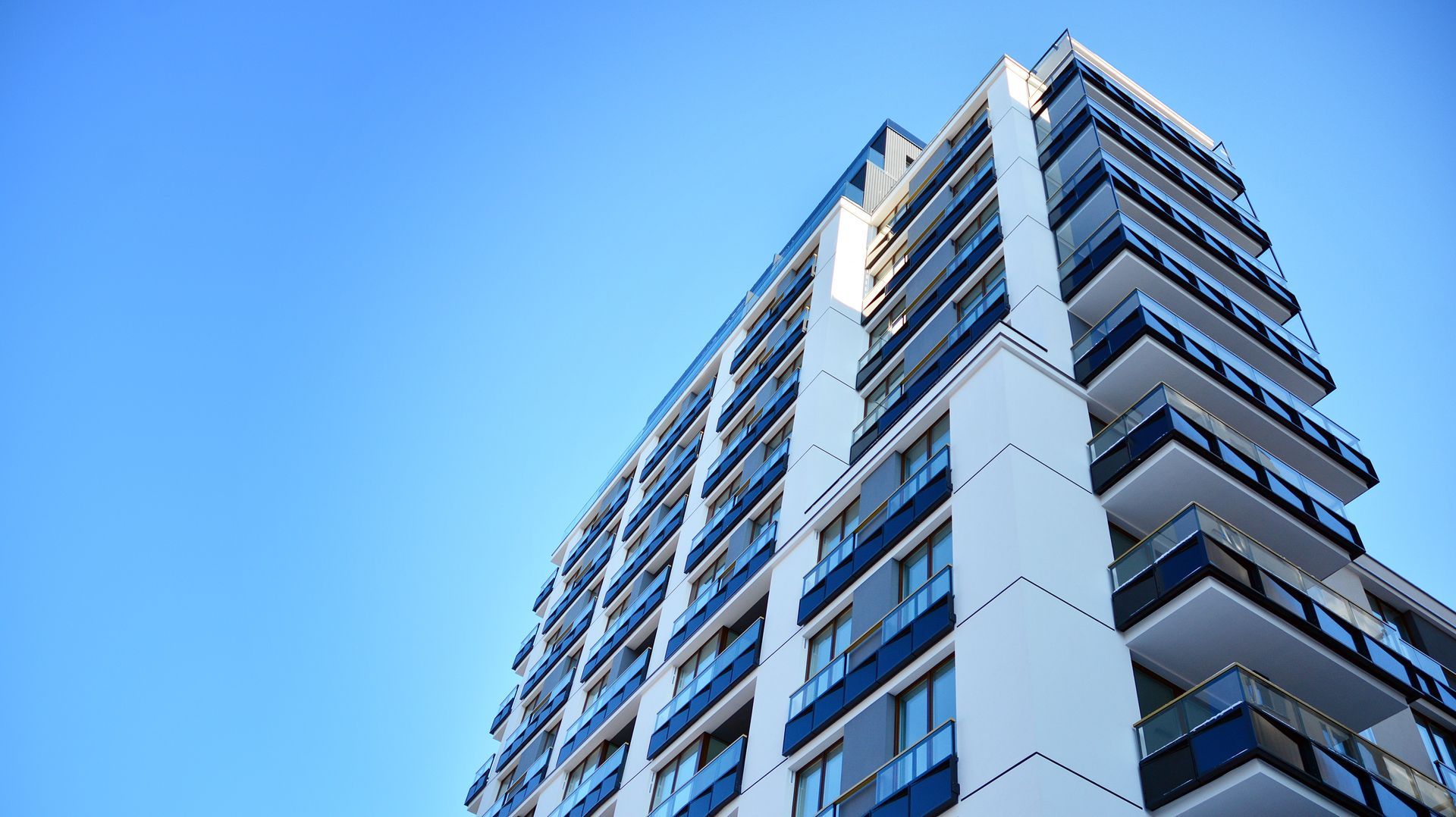 Modern high-rise apartment building with balconies against a clear blue sky