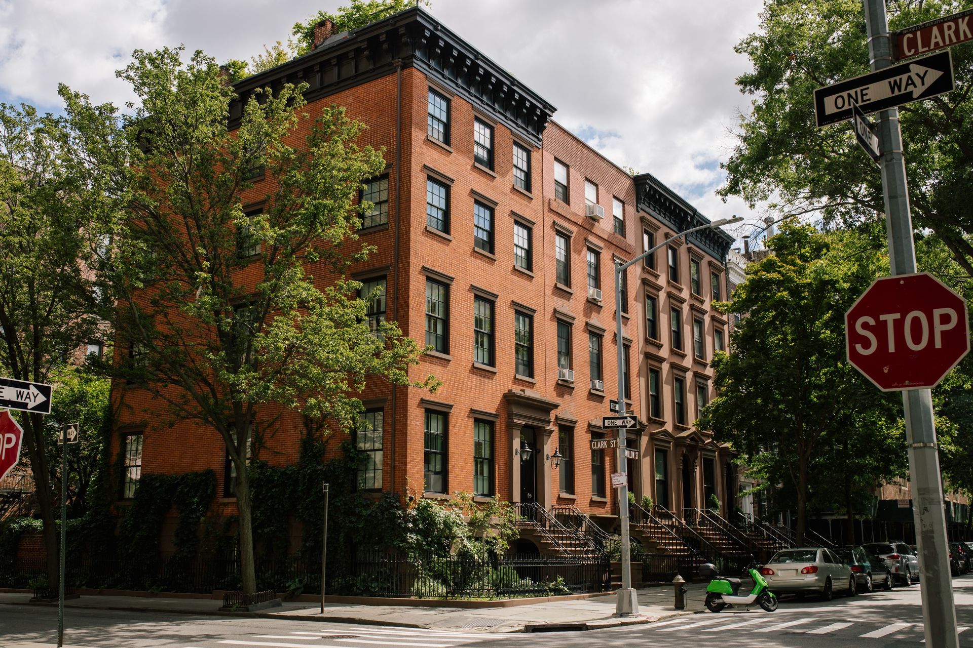Tree-lined city street with brick rowhouses, a stop sign, and cloudy sky