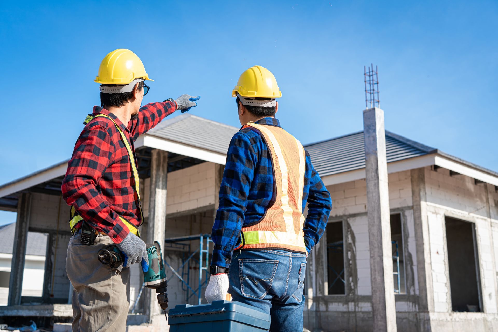 Two construction workers in hard hats inspecting a house under construction outside
