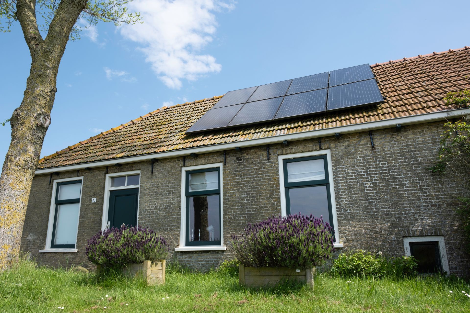 Stone house with solar panels on the roof and a grassy front yard under a blue sky