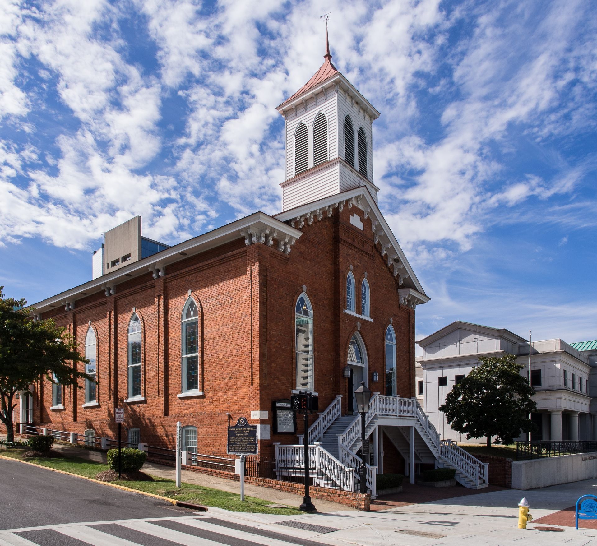 Red brick church with white steeple on a sunny street corner under a blue sky
