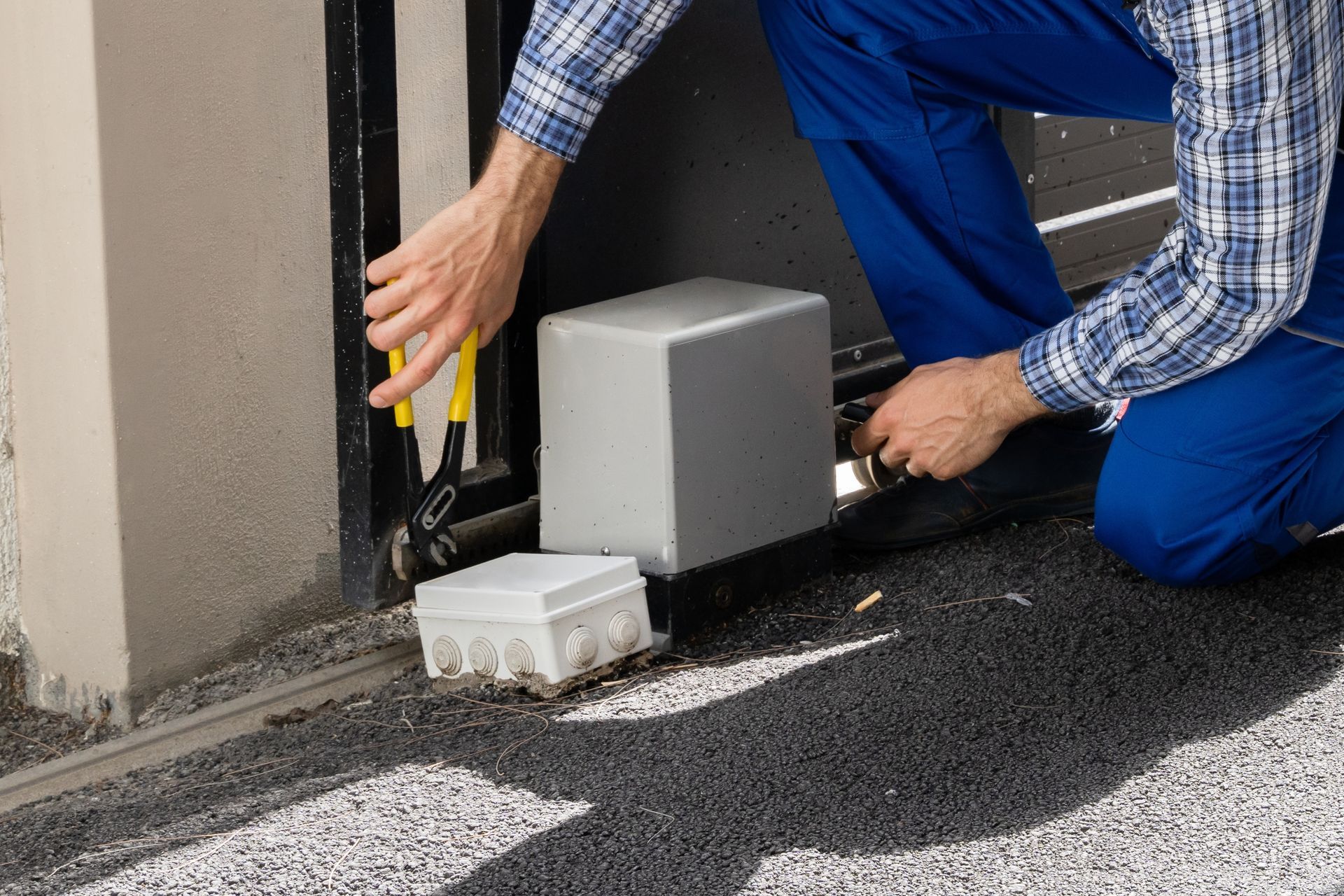 Worker installing a gray electrical box along a wall with tools on the ground