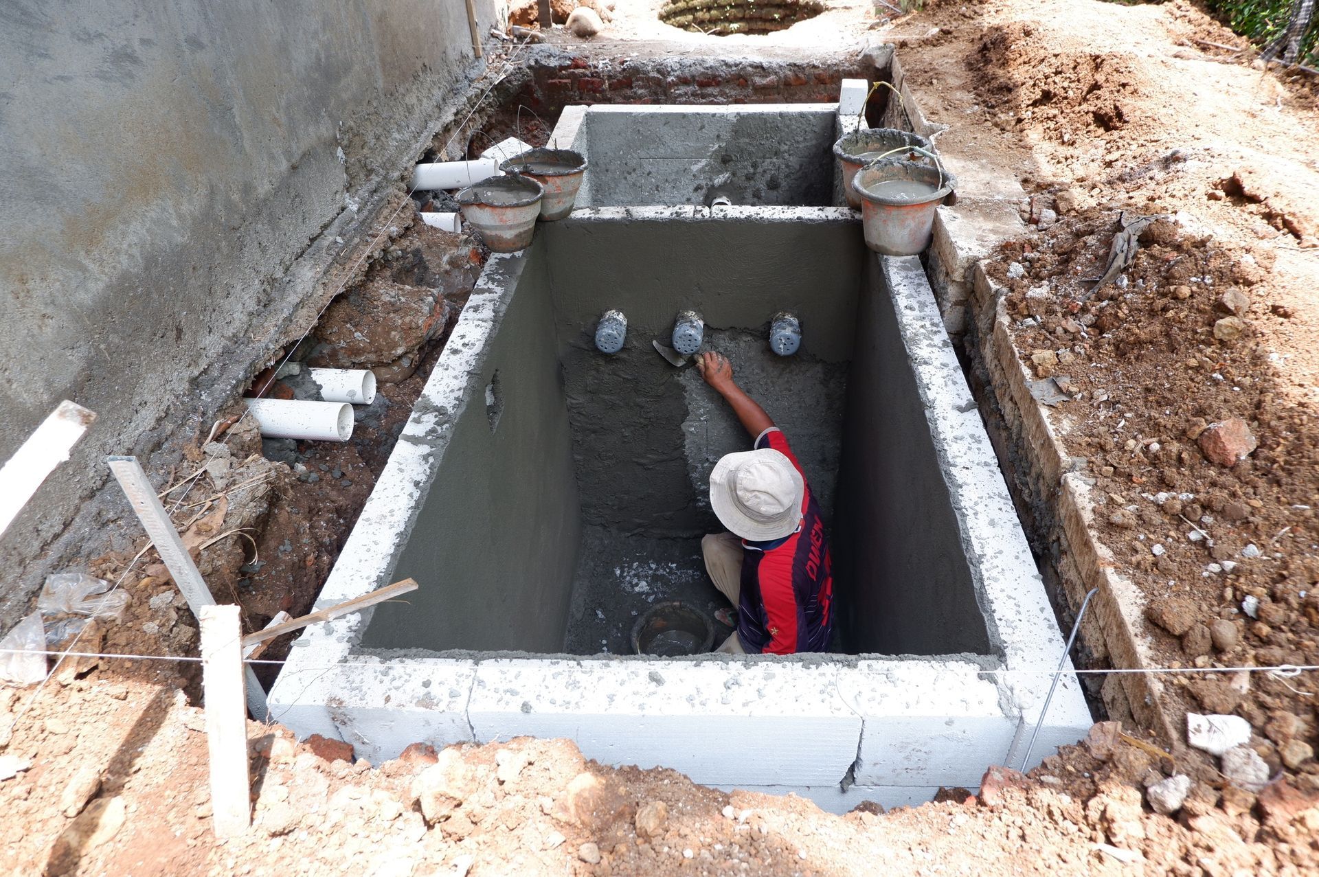 Worker in a trench inspecting underground pipes and concrete utility vault during construction