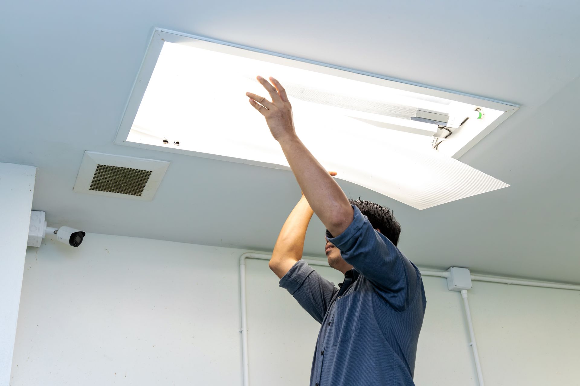 Person reaching up to open a ceiling light panel in a white room.