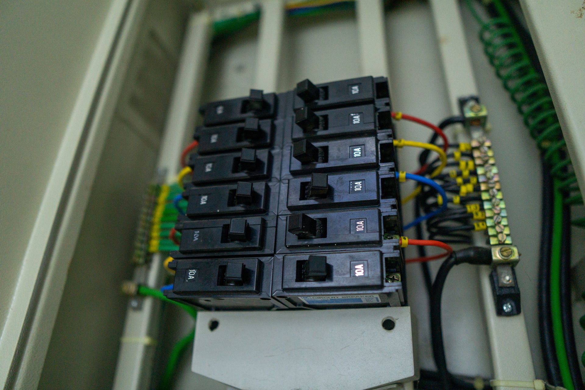 Electrical breaker panel with rows of black switches and multicolored wiring inside a cabinet