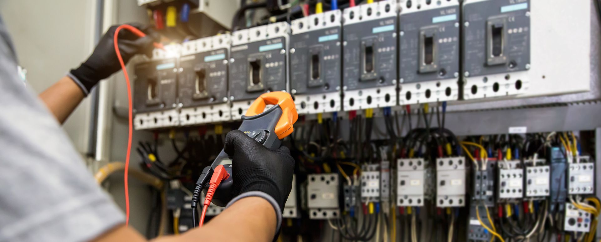 Technician wearing orange gloves adjusts wiring in an electrical control panel.