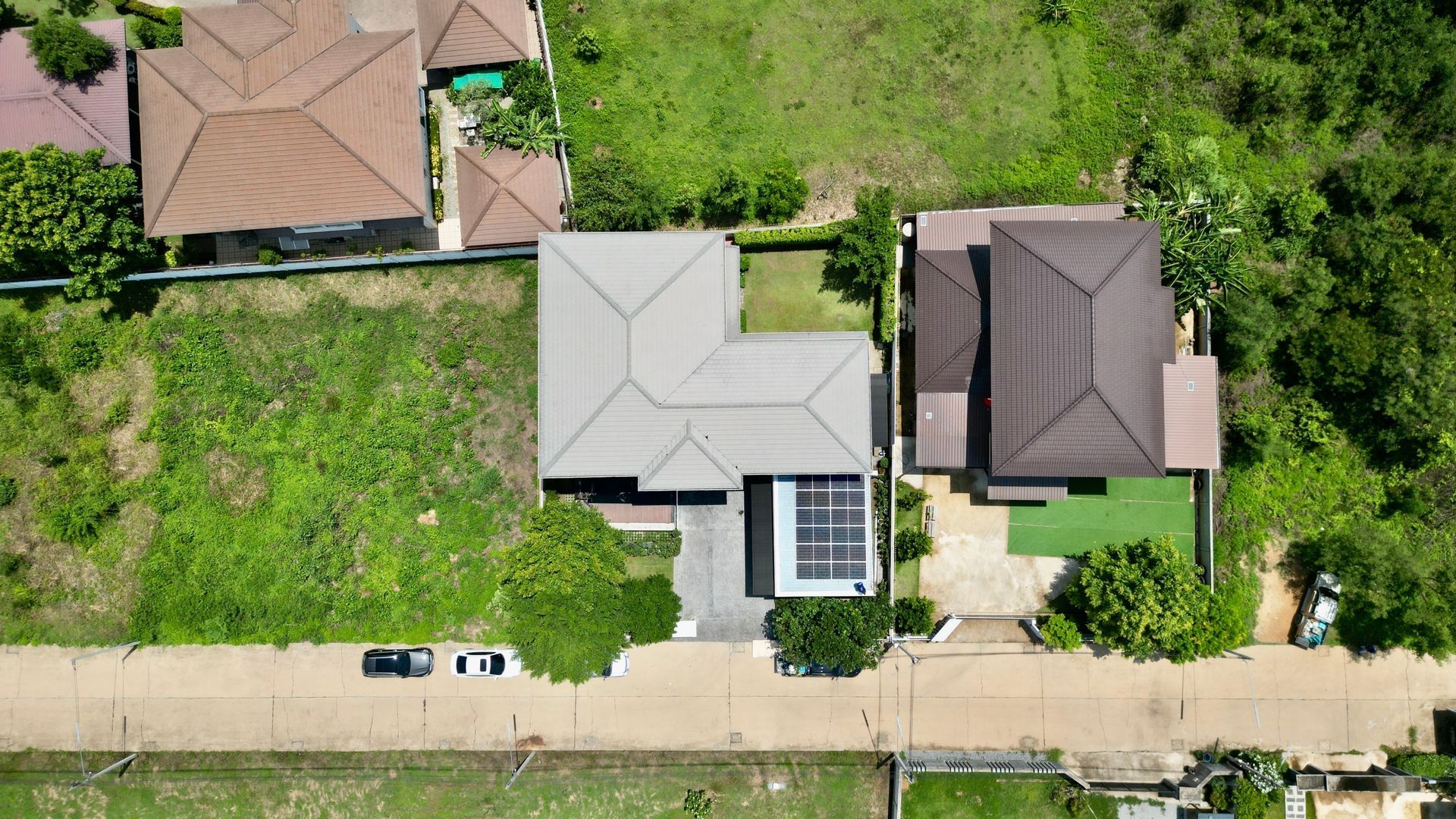 Aerial view of three houses with lawns and parked cars along a residential street.