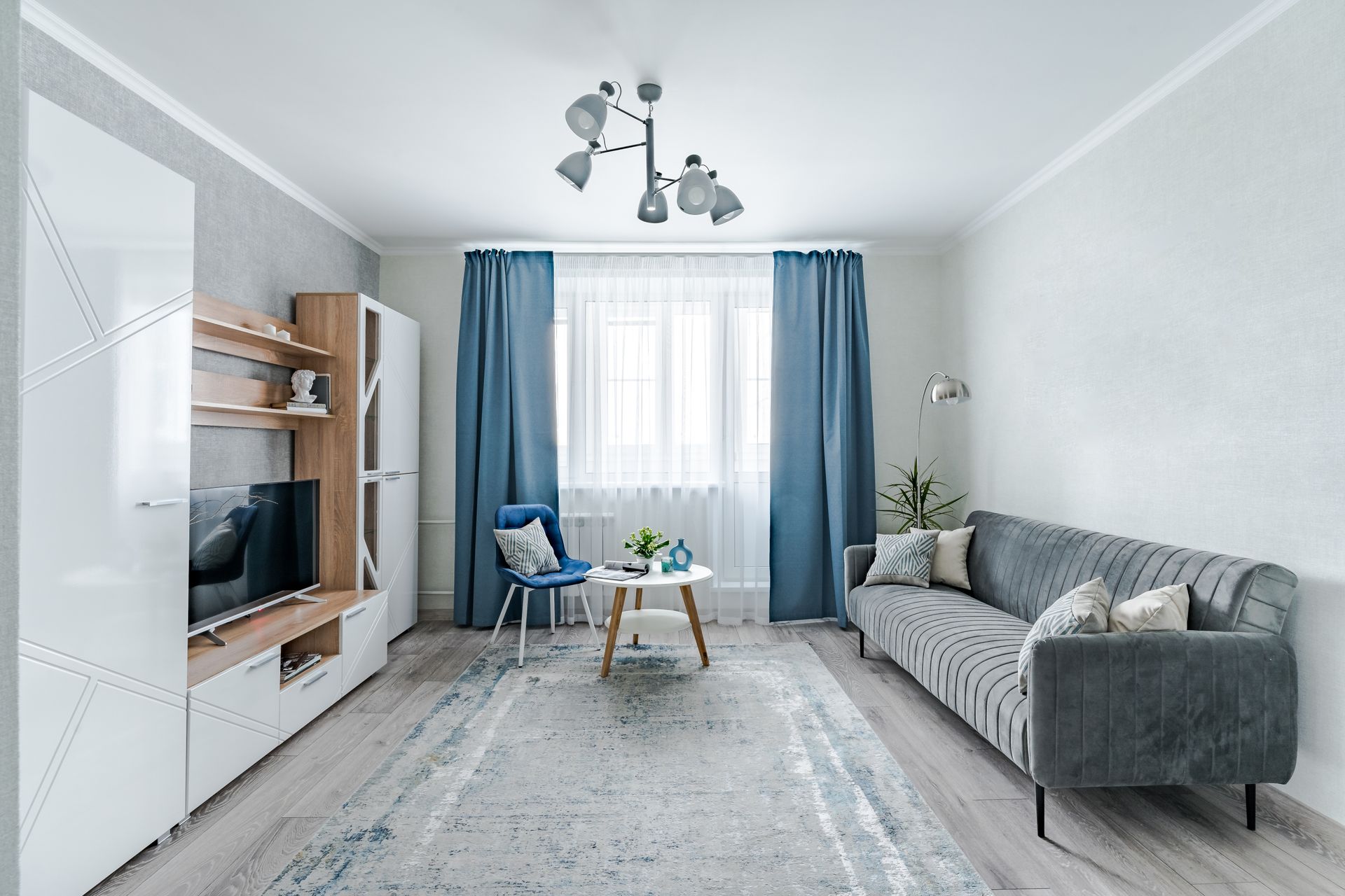 Bright living room with gray sofa, TV stand, blue curtains, and coffee table by a window.